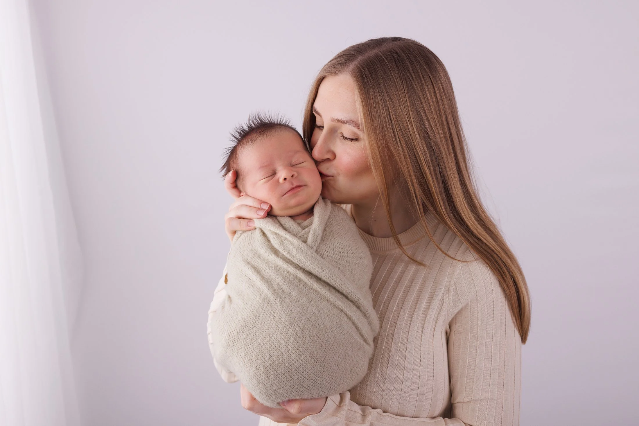 Mom in a cream top holding baby wrapped in soft green
