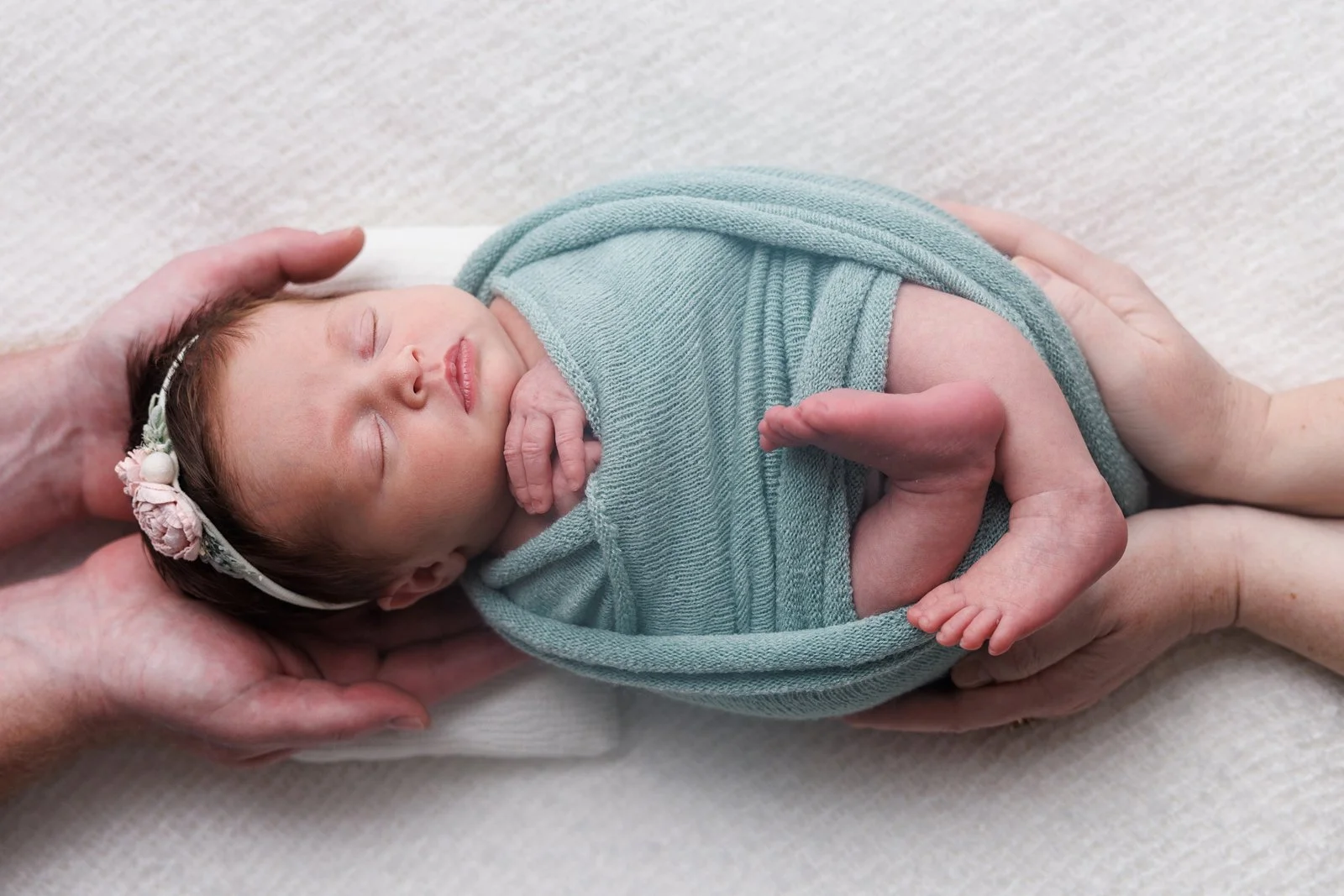 parents holding newborn baby wrapped in green