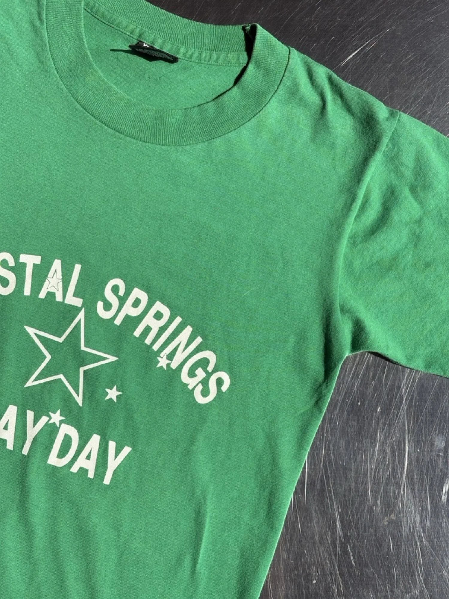 Close-up of white arched Crystal Springs Play Day lettering and star print on vintage green t-shirt