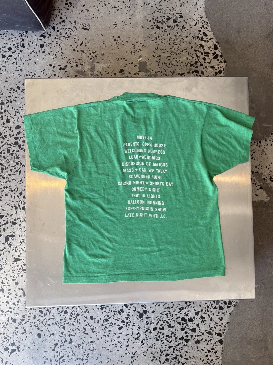 Vintage green Orientation Committee t-shirt laid flat, back view showing printed event schedule