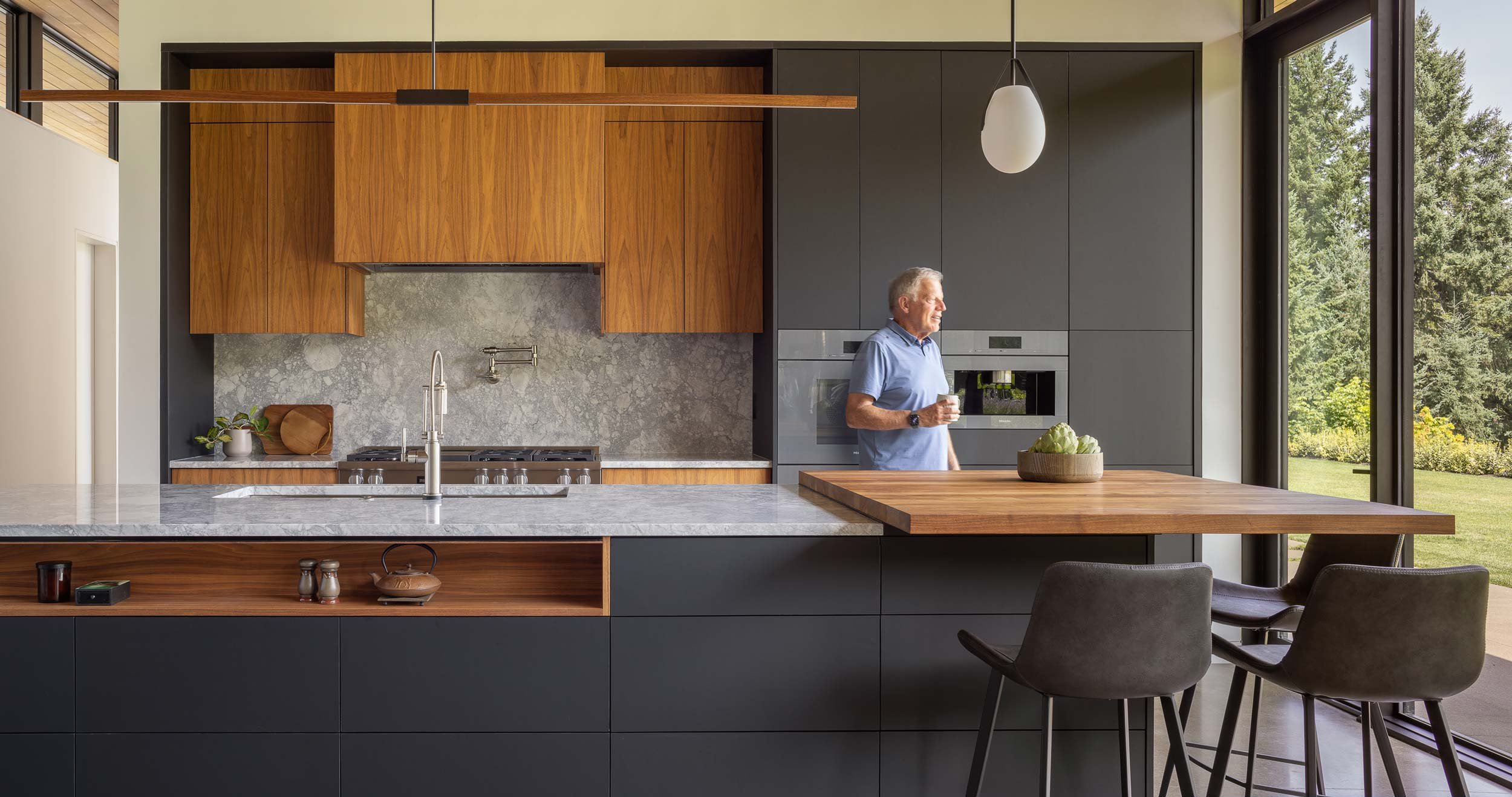 Man in kitchen with gray and wood cabinets and marble countertop