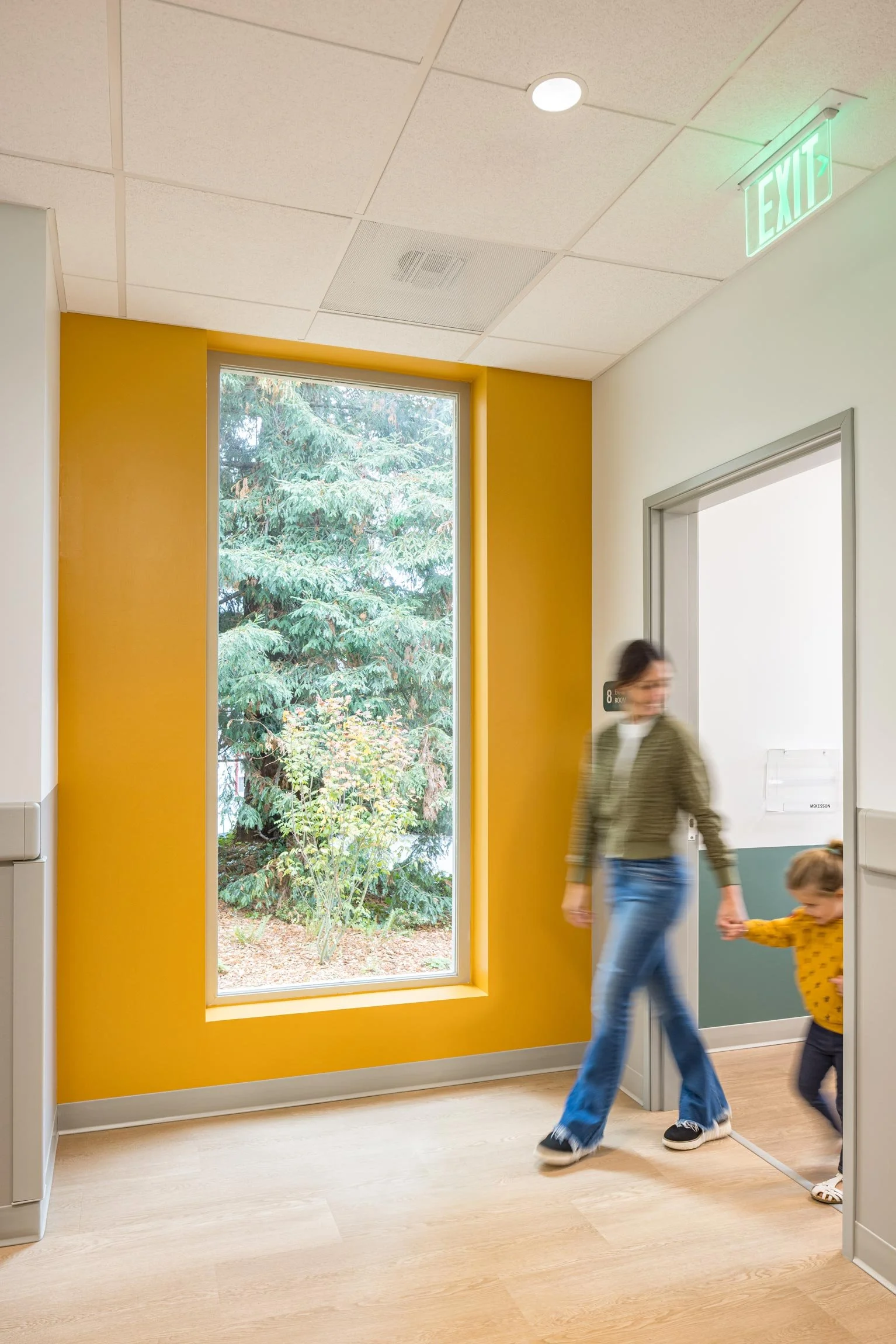 Mother and daughter leaving exam room into hall with yellow wall