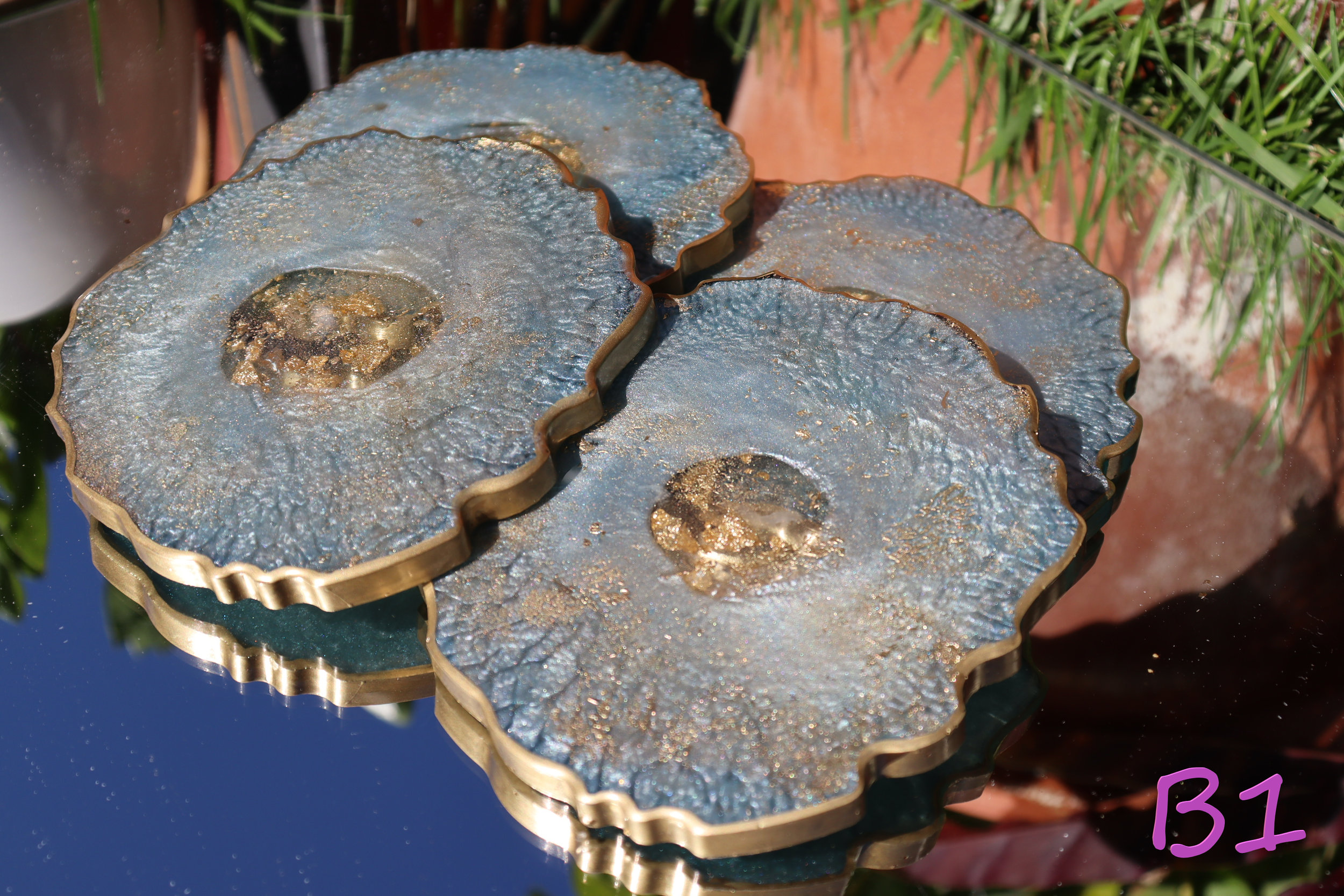 Close-up of mineral samples with blue and gold hues, stacked in a metal container, with green plants in the background.