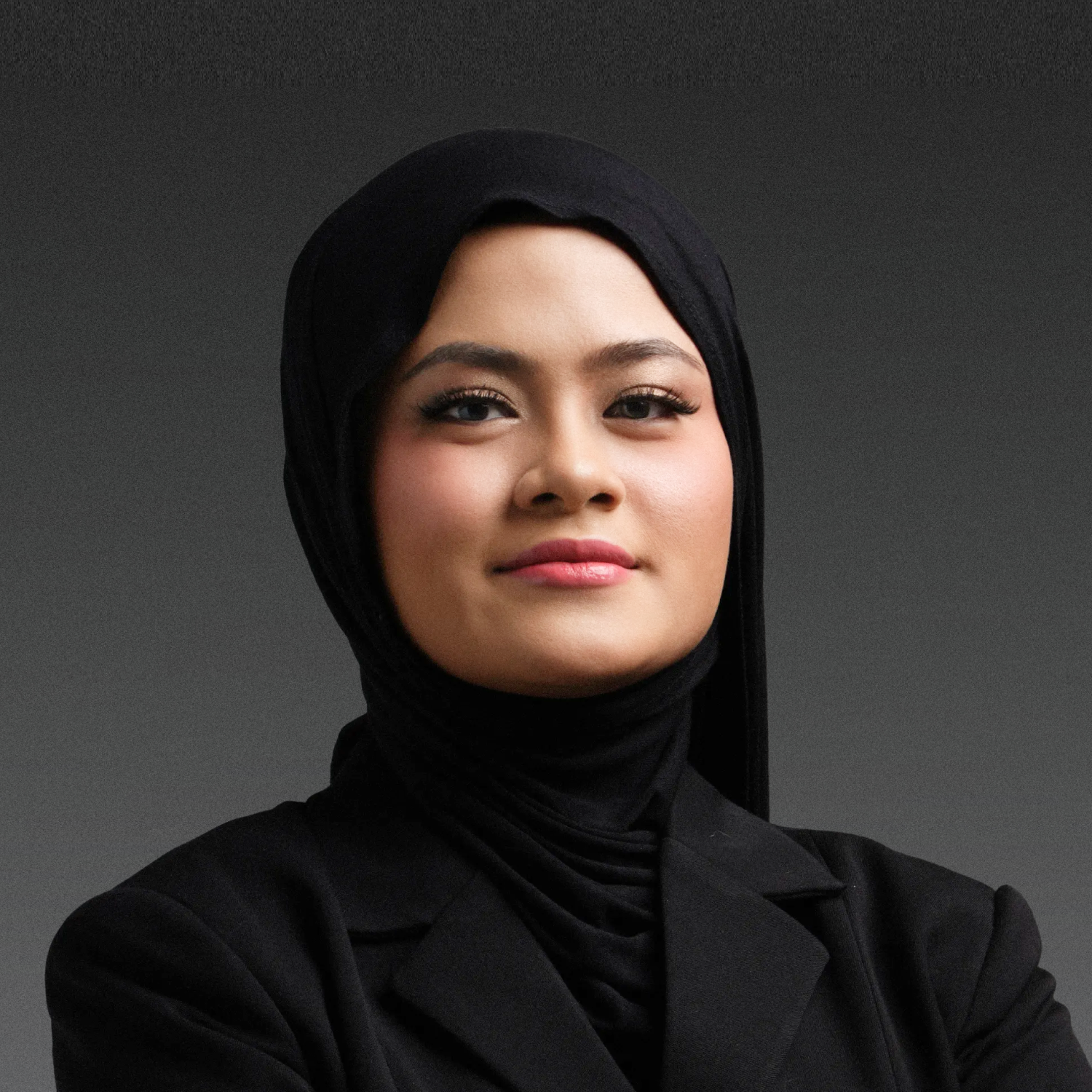 Portrait of a person wearing a black hijab and a dark gray top against a light gray background.