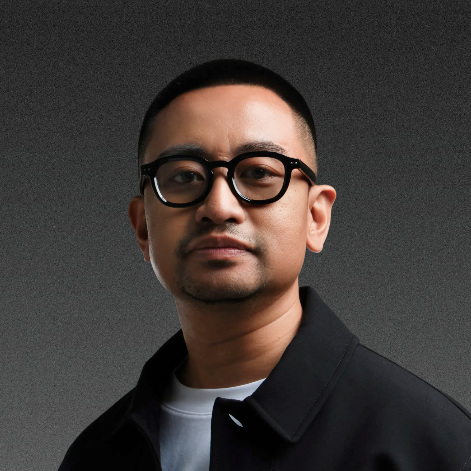 Smiling person with glasses and short hair wearing a black jacket.