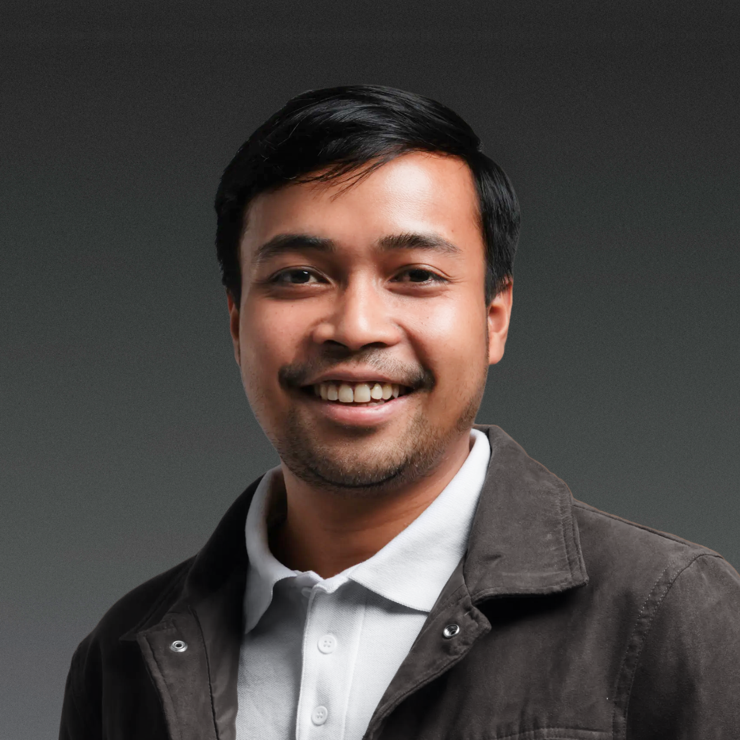 Smiling person wearing a dark jacket over a light shirt, against a plain background.