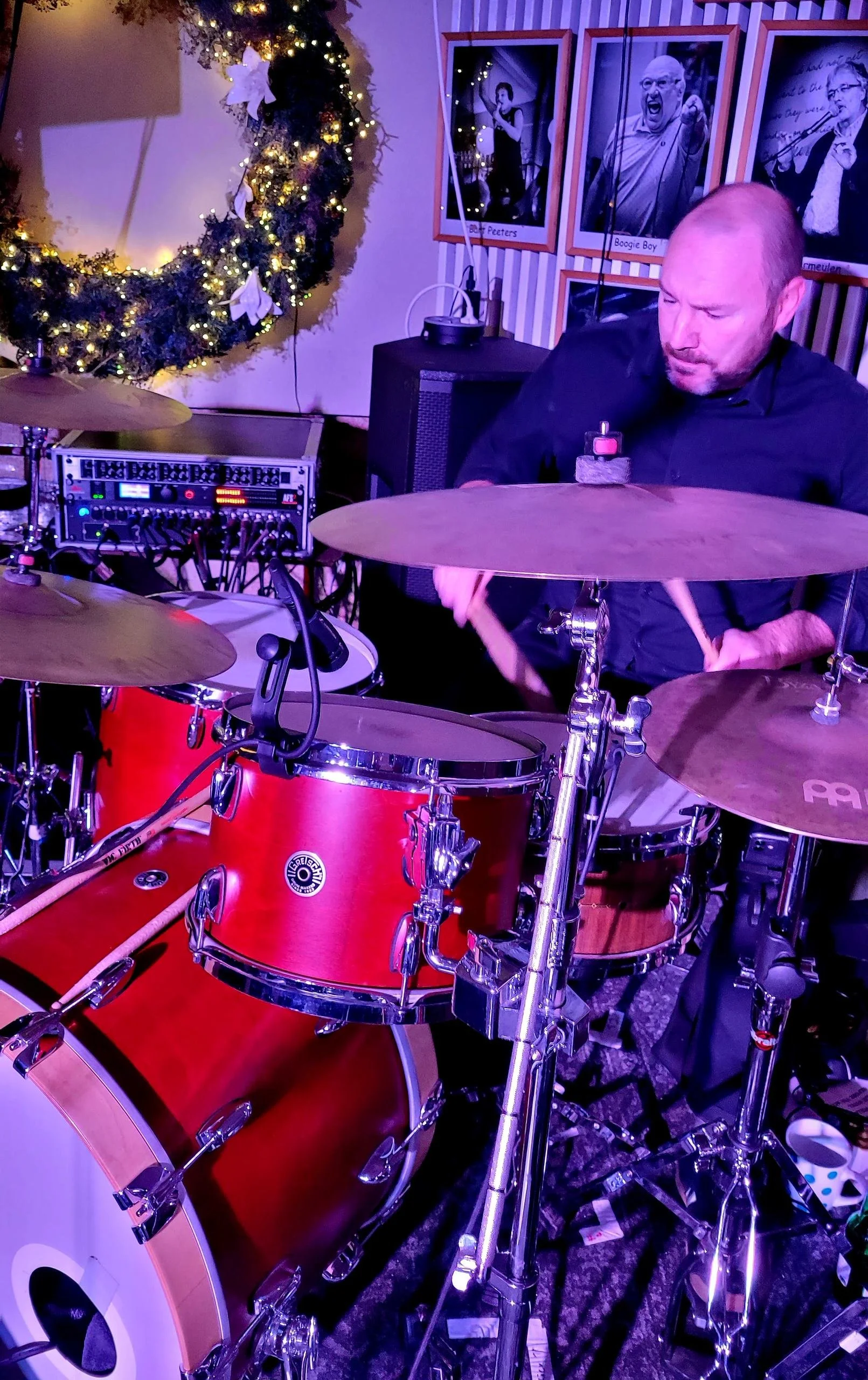 Man die op drums speelt in een ruimte met kerstversiering en foto's aan de muur.