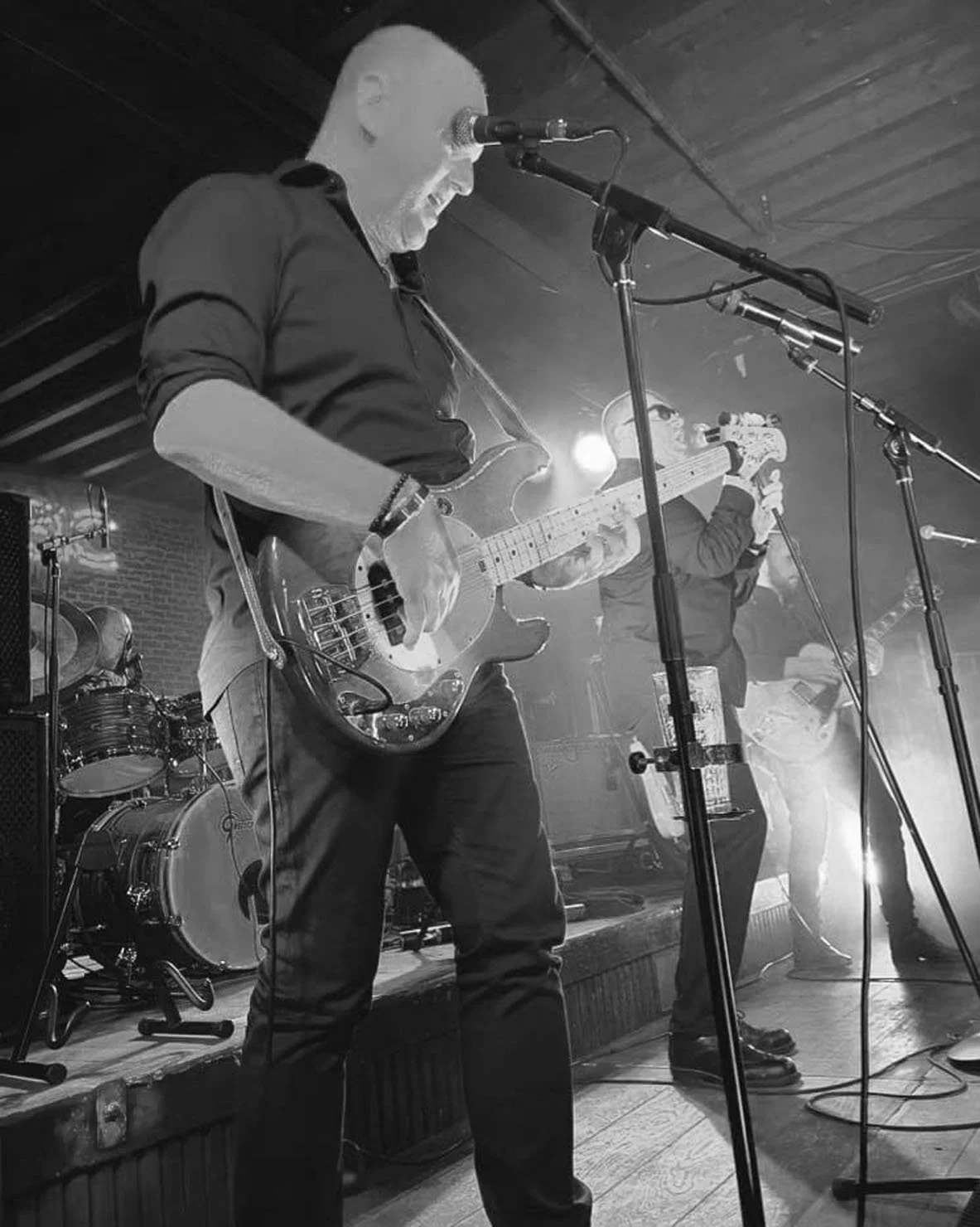 Mannen met een basgitaar en een andere artiest met een microfoon op een podium tijdens een live muziekoptreden.