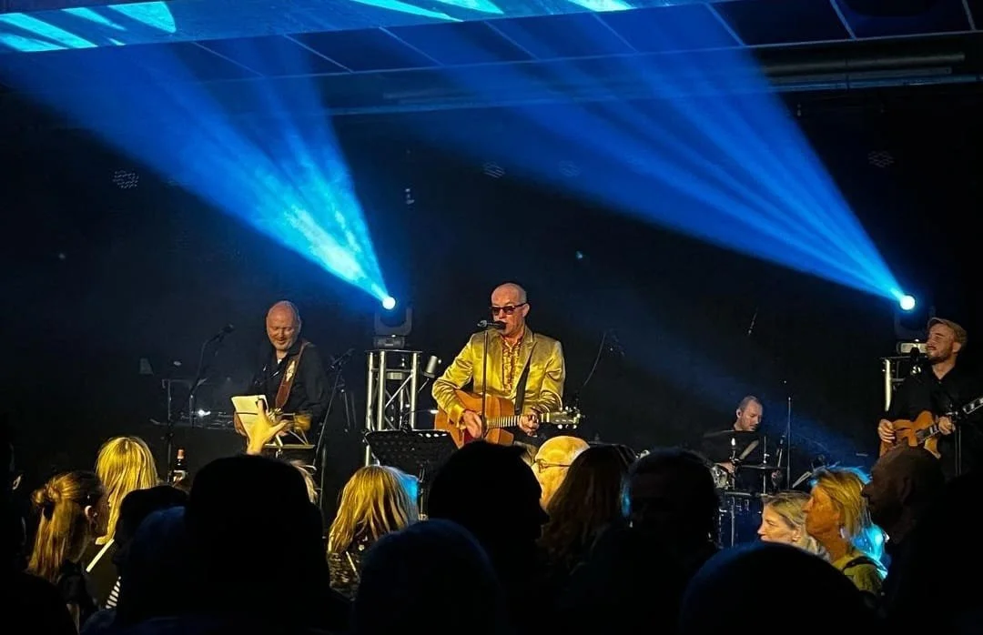 Mannen die live muziek spelen op een podium met blauwe spots en publiek in de voorgrond.