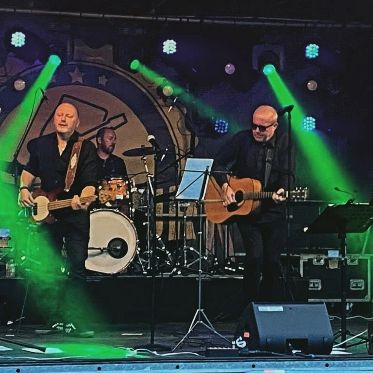 Muziekband speelt op een podium met muzikanten die gitaren en drums bespelen, verlicht door groene spotlights.