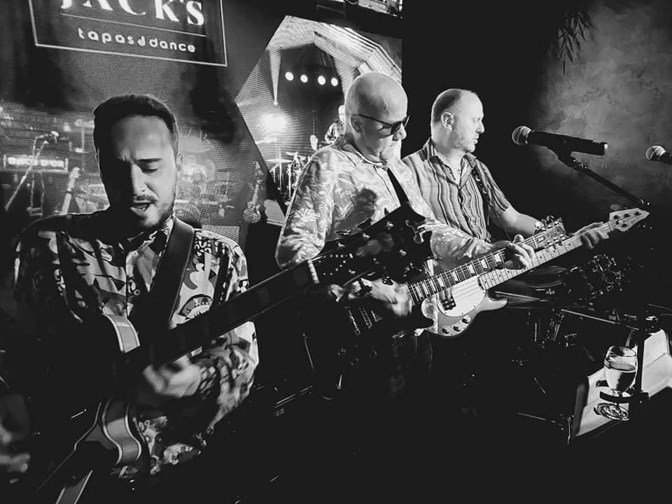 Drie muzikanten spelen akoestische gitaren op een podium tijdens een live optreden in een bar of club.