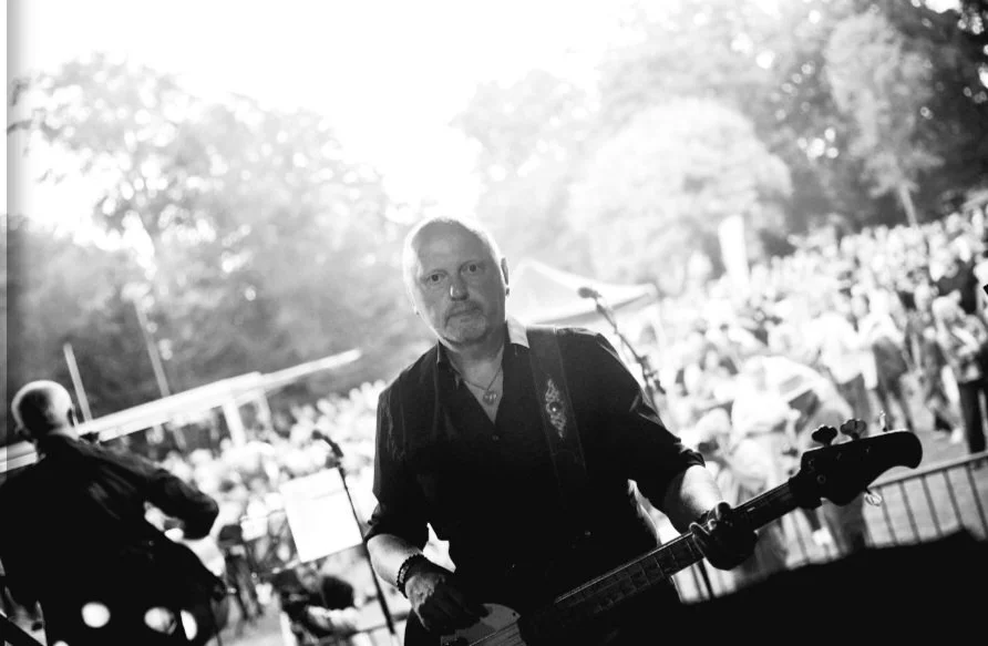 Mann met een gitaar op een buitenfestival, omgeven door een grote menigte.
