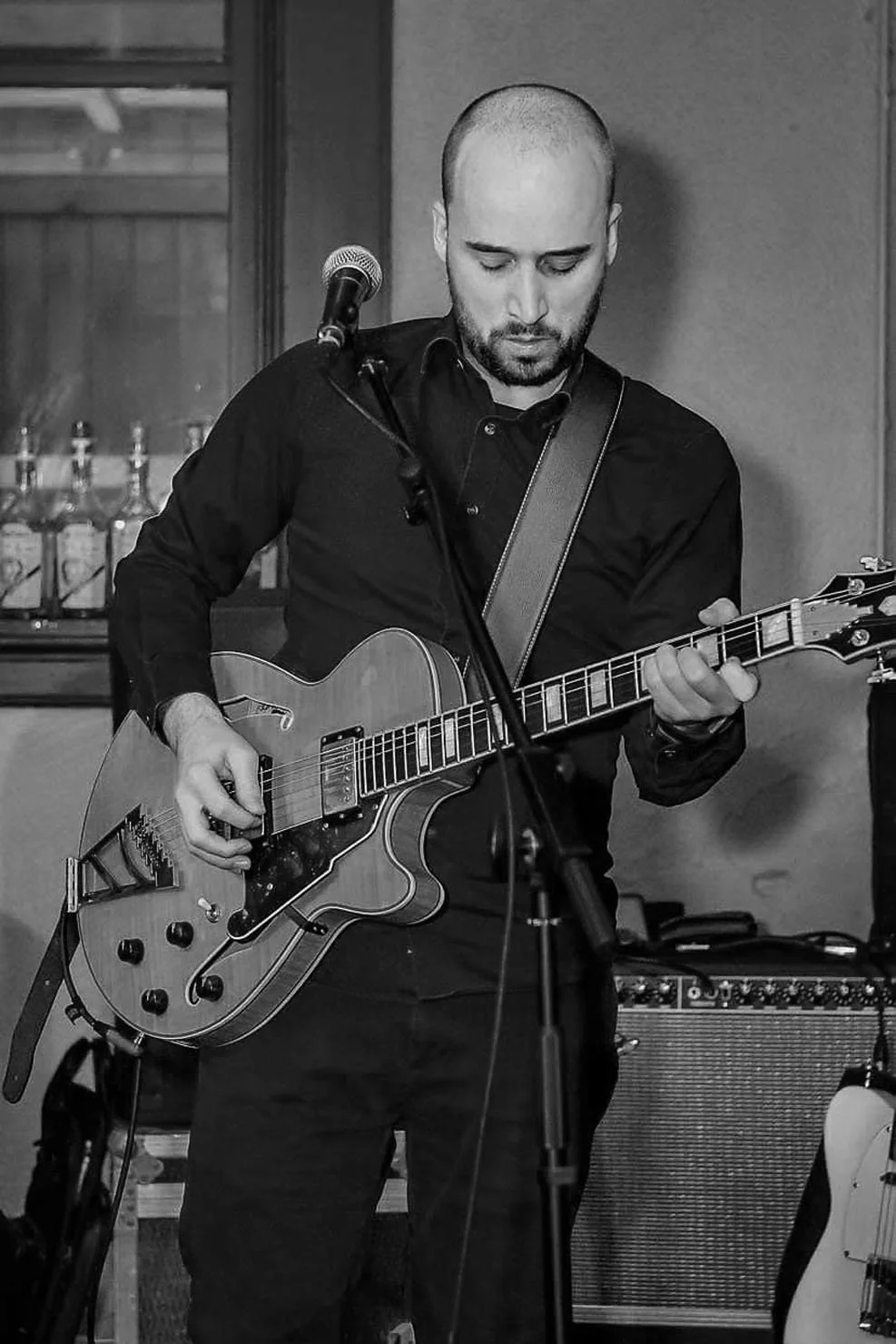 Man speelt gitaar bij een microfoon in een binnenruimte, zwart-wit foto.