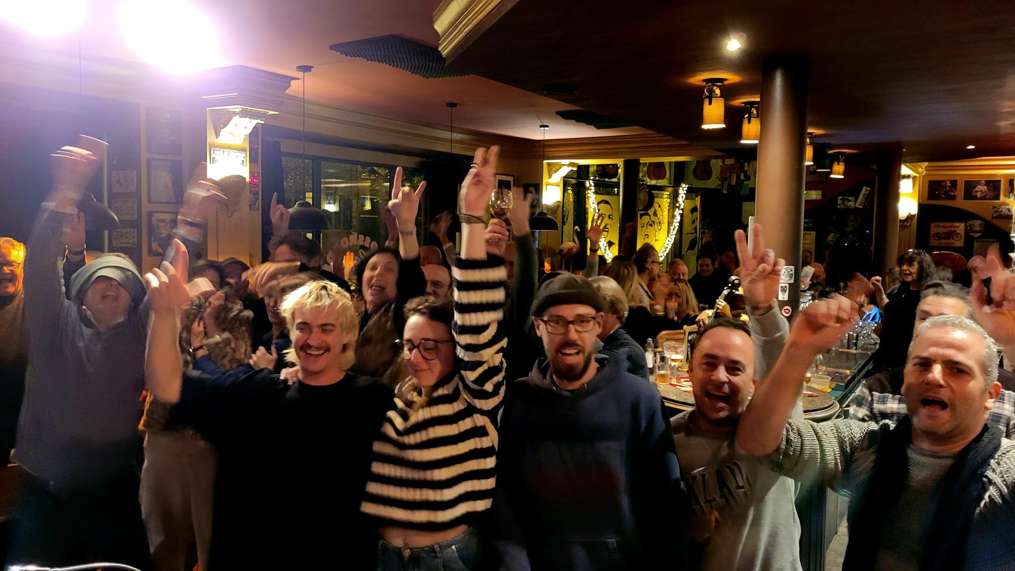 Feestvierders in een café of restaurant die juichen en feest vieren, met sommige mensen met opgestoken handen en één persoon met een glas wijn.