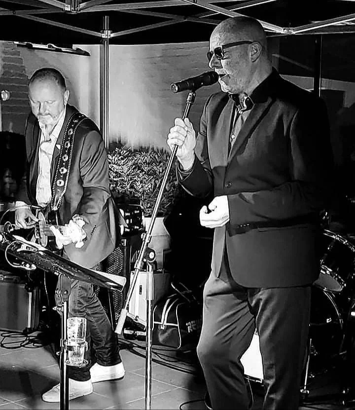 Twee muzikanten spelen live op een podium, een zanger met een microfoon en een gitarist, zwart-w white afbeelding.