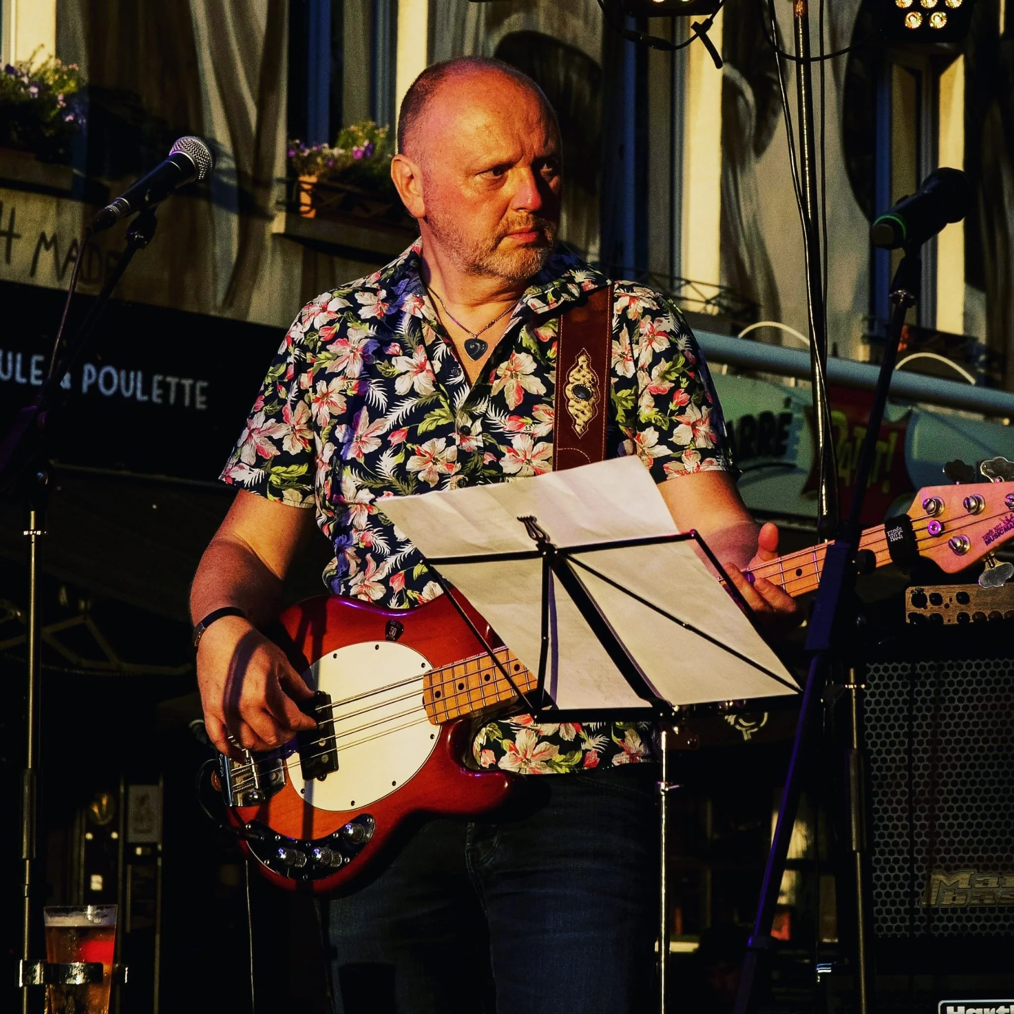 Een man met een bloemen shirt speelt basgitaar tijdens een live optreden in een restaurant of café.