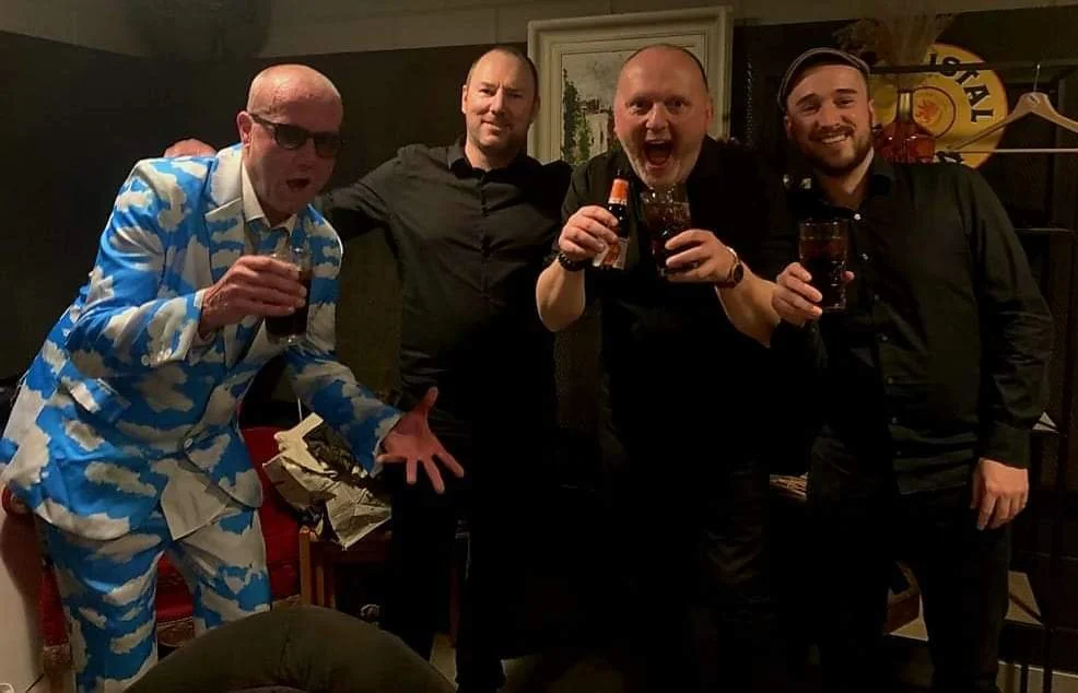 Vier mannen vieren feest met drankjes in een gezellige kamer.