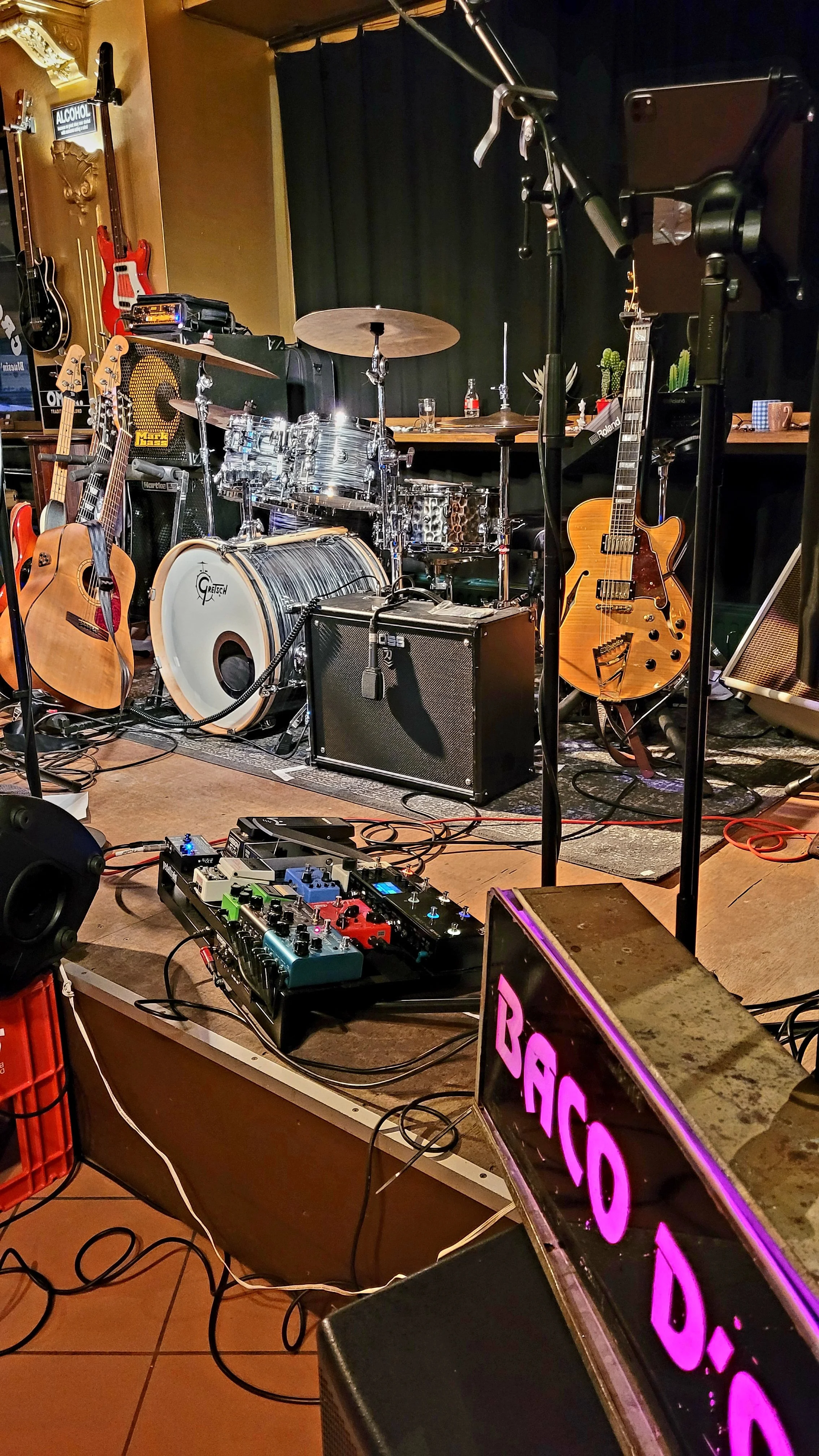 Muziekinstrumenten en apparatuur opgesteld op een podium, klaar voor een optreden, inclusief gitaren, een drumstel, een versterker en een DJ-controller.