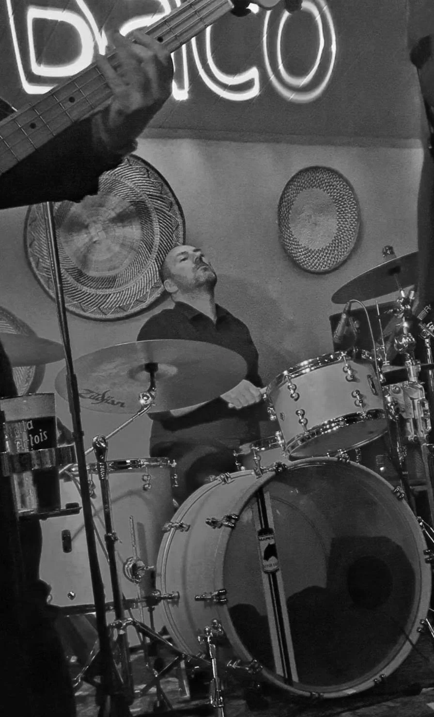 Een man speelt drums in een muzieksessie, met een andere muzikant die een gitaar speelt.