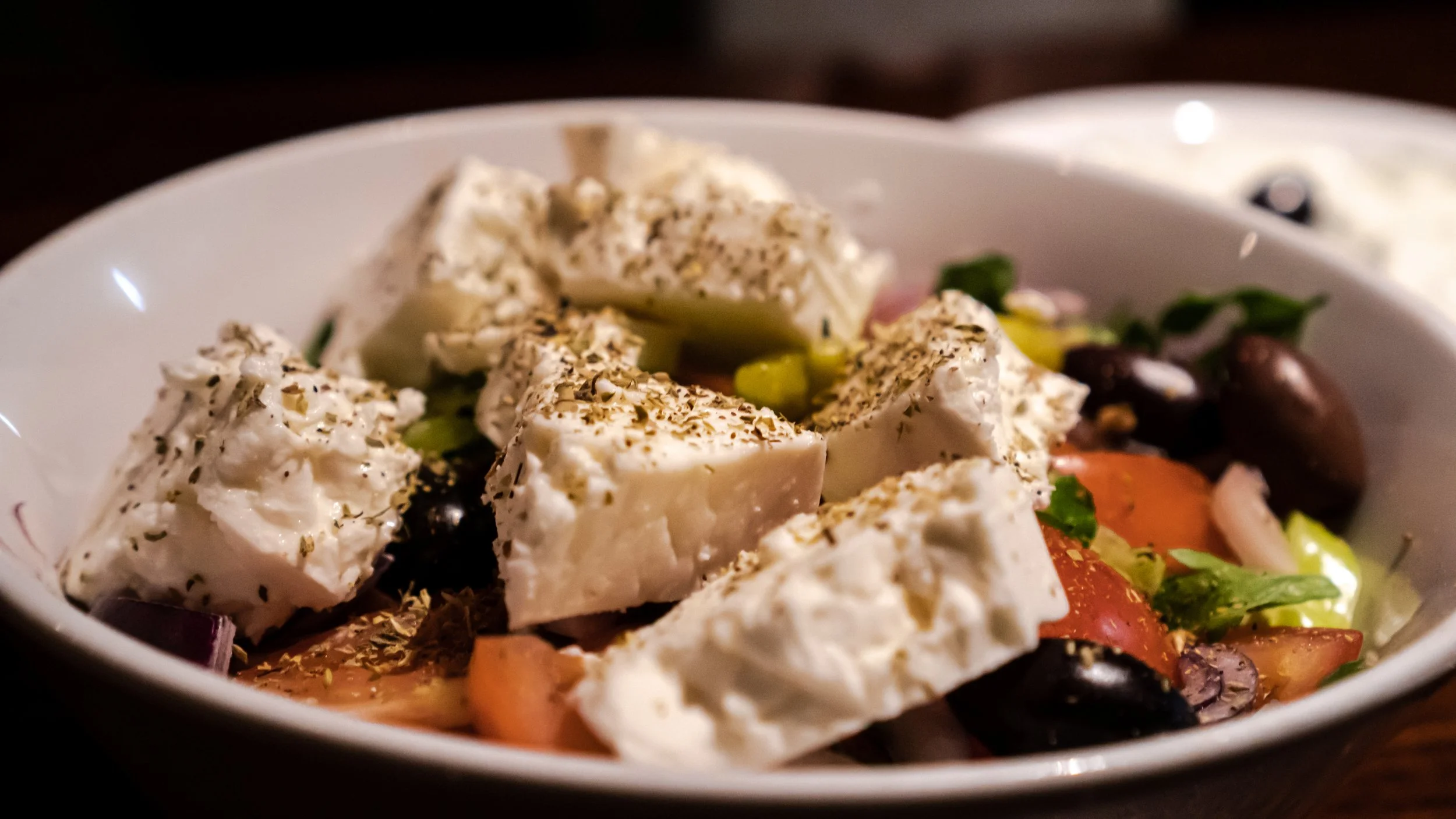 Greek salad with feta cheese, cherry tomatoes, black olives, cucumbers, and herbs in a bowl.