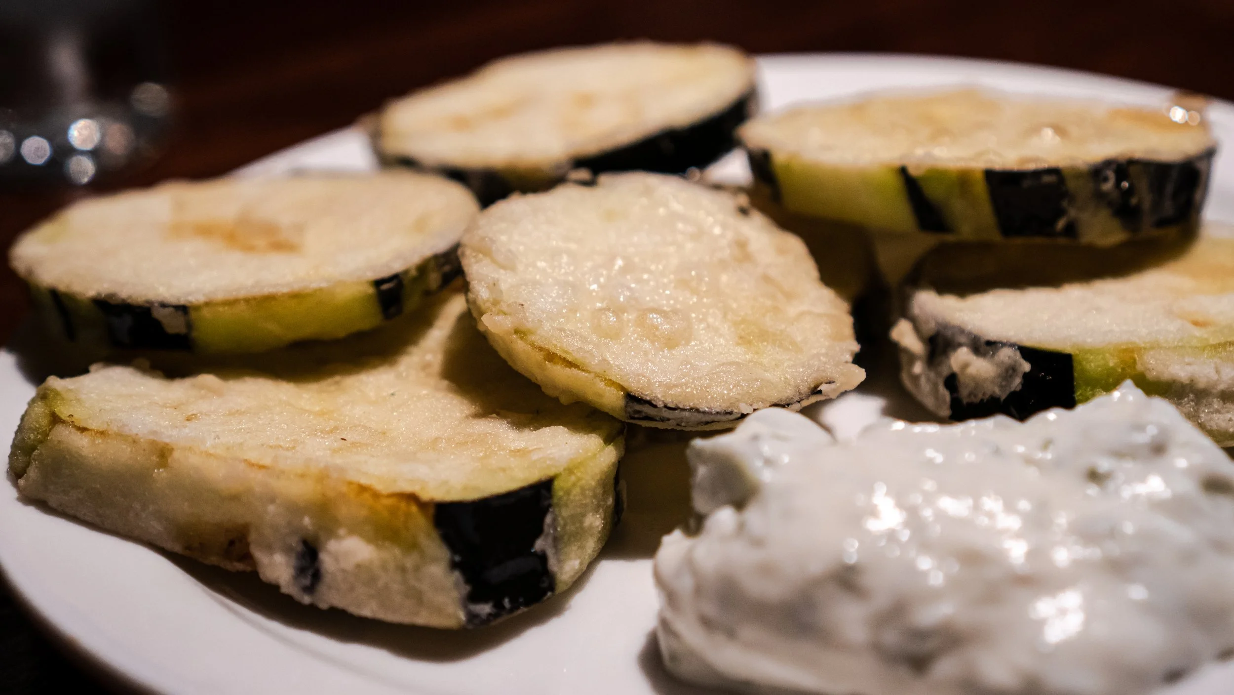 Slices of eggplant with a creamy tzatziki sauce on a white plate.