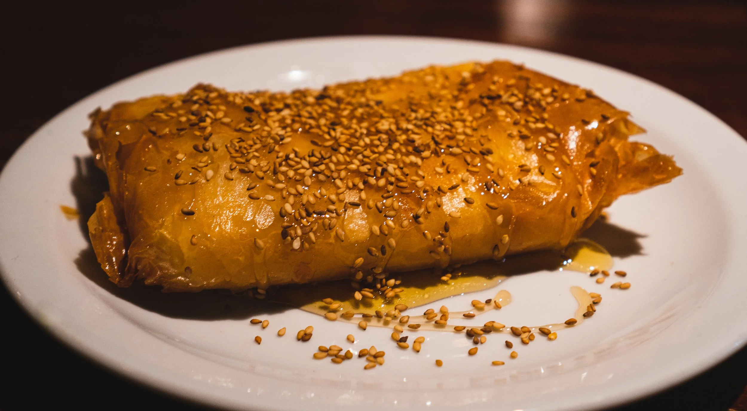 A plate with a golden-brown pastry topped with sesame seeds, drizzled with honey.