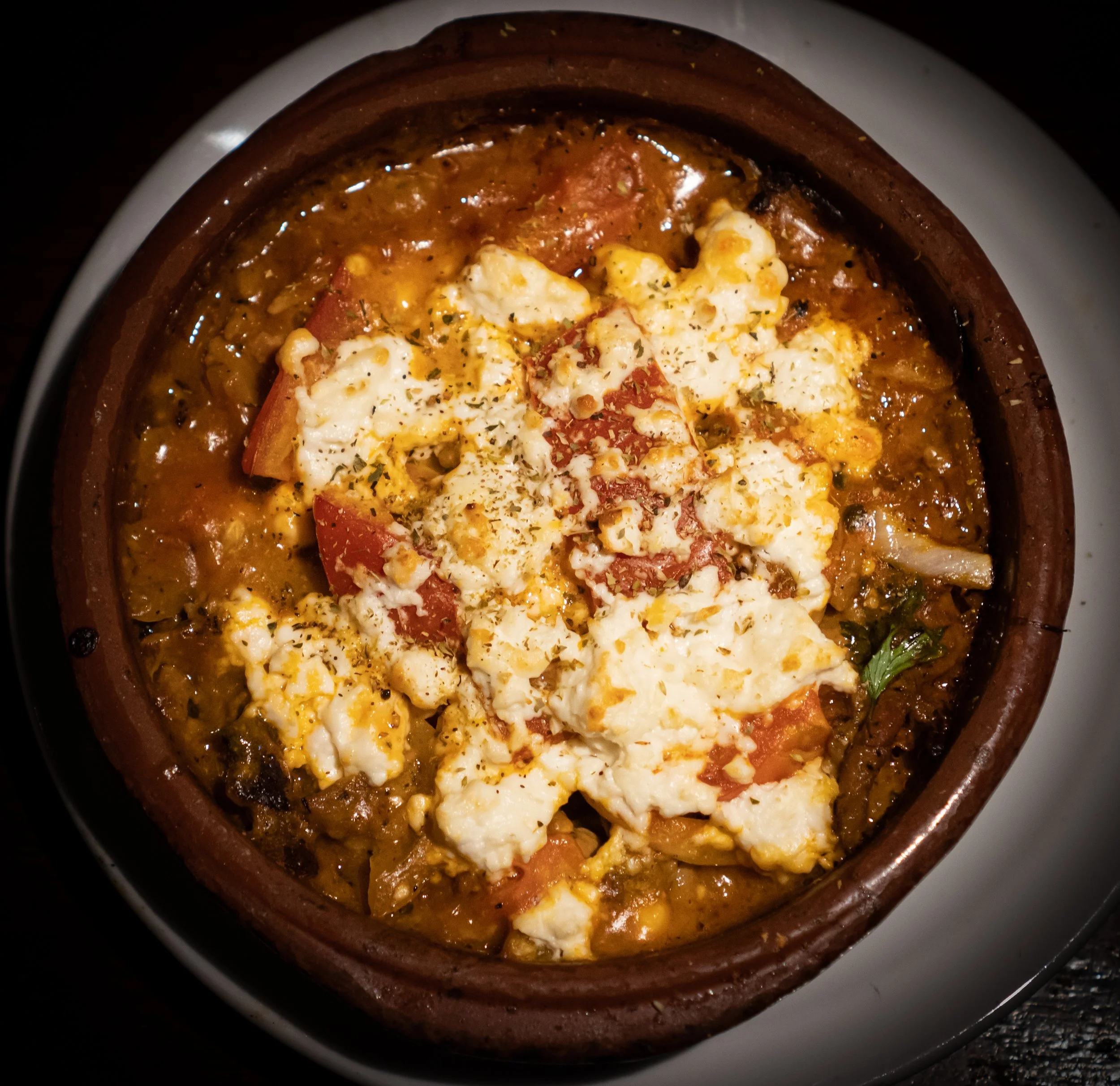 A baked dish in a ceramic pot with melted cheese, tomato, and herbs