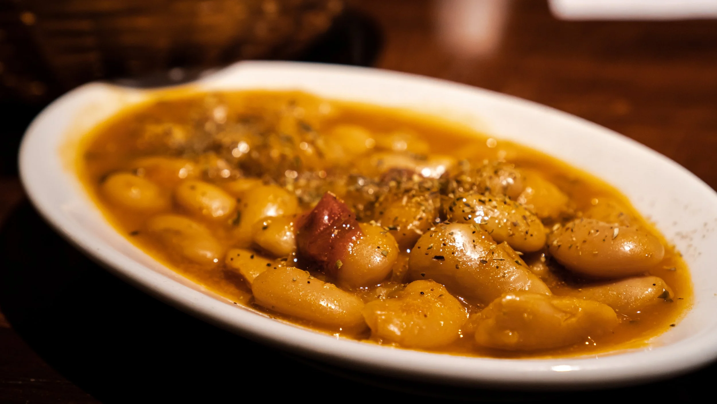 A white oval bowl filled with yellow beans in a broth, garnished with herbs and spices.