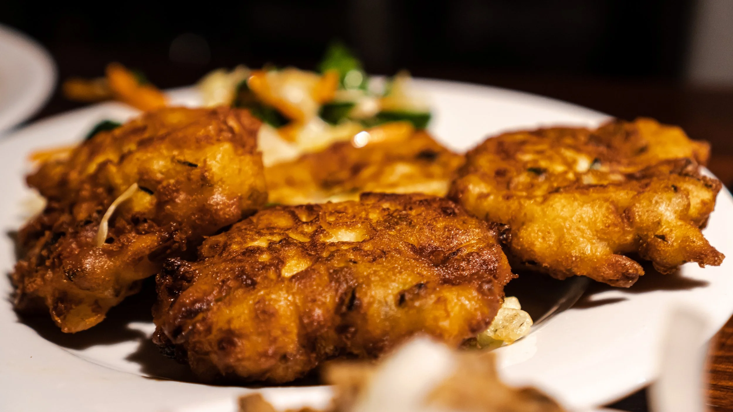 Fried zucchini balls served on a white plate with mixed vegetables in the background.