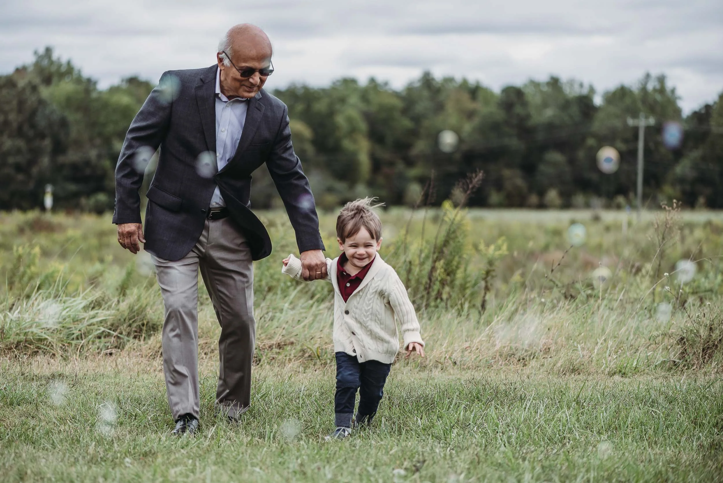 grandfather and toddler playing with bubbles in field during extended family photo session in charlotte north carolina