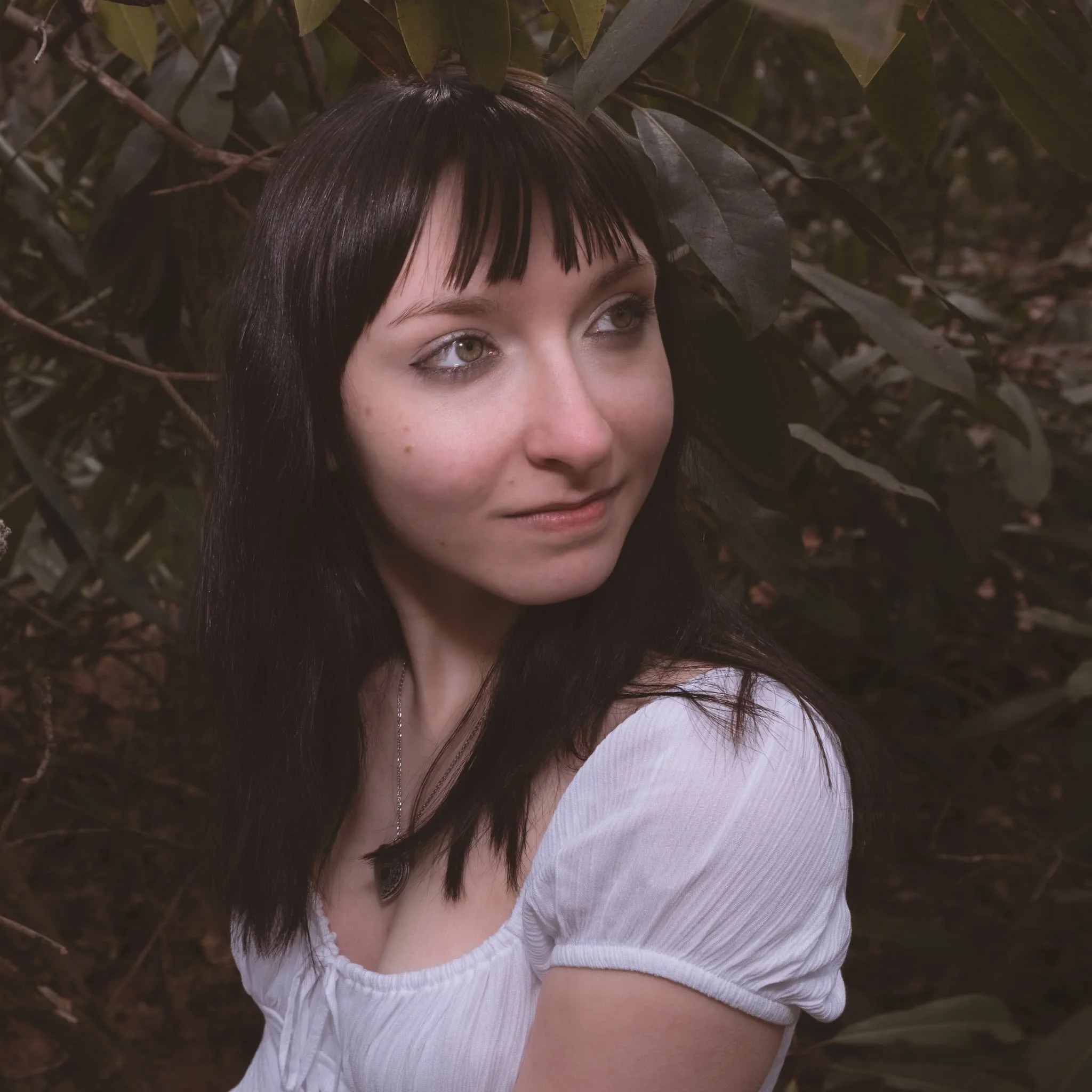 Outdoor portrait session photographed in Scranton, Pennsylvania. Moody natural light filters through dark foliage as the subject gazes softly off-frame — an intimate, editorial-style portrait that feels more discovered than posed. Paulette Michelle P