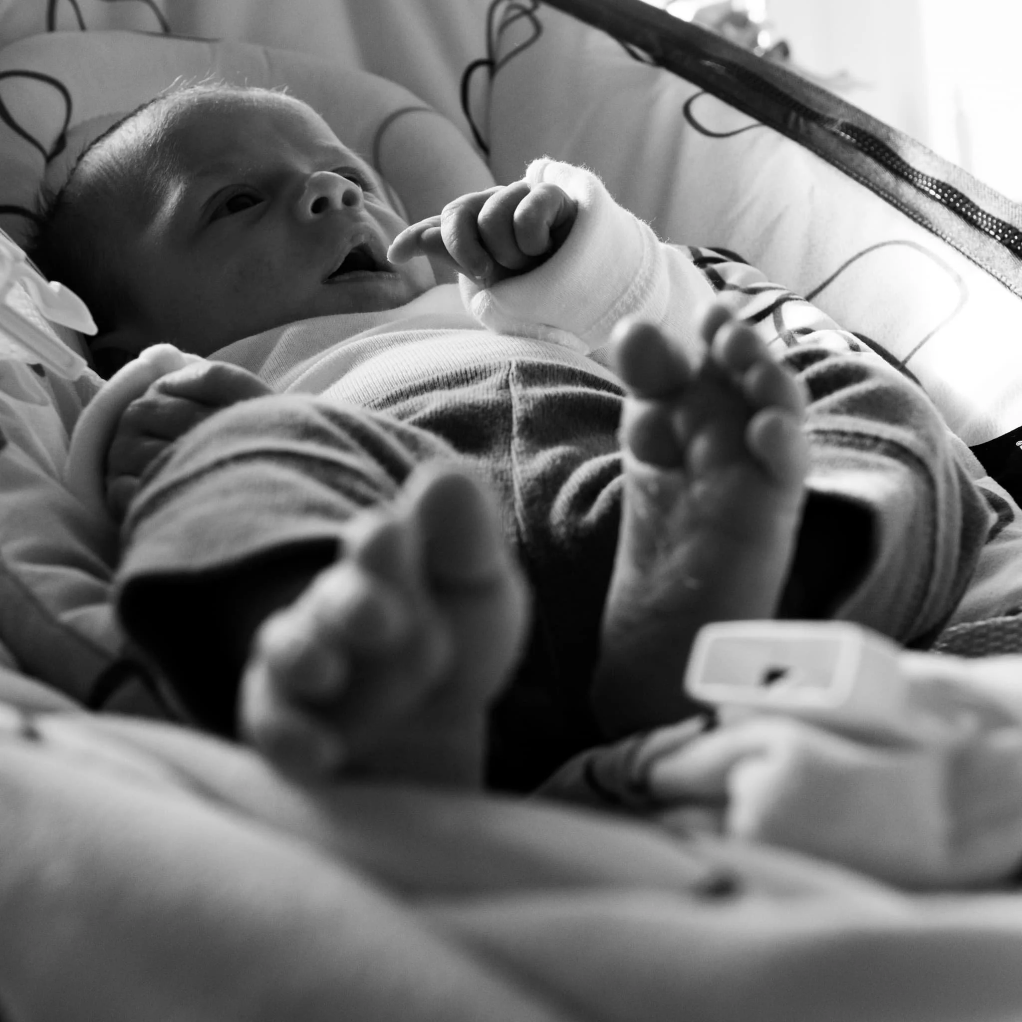 Black and white newborn portrait captured during an in-home lifestyle newborn session in Northeastern Pennsylvania. Tiny bare feet and curled fists fill the frame, telling the whole story of new life in a single breath. Paulette Michelle Photography 