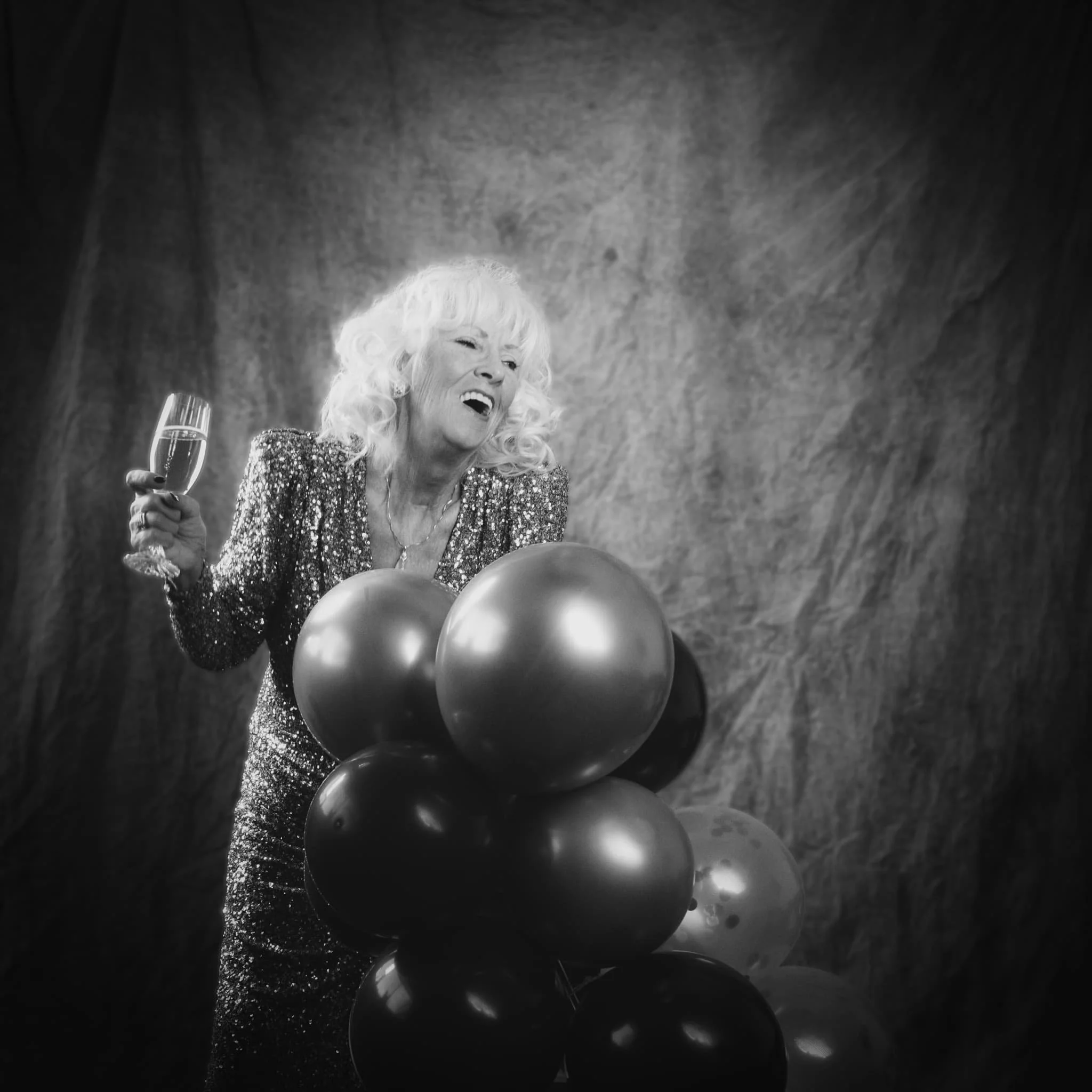 Black and white studio portrait session photographed in Wilkes-Barre, Pennsylvania. Pure joy — a woman in a sequined dress laughing mid-celebration, champagne glass raised, surrounded by balloons. Paulette Michelle's Wilkes-Barre studio is available 
