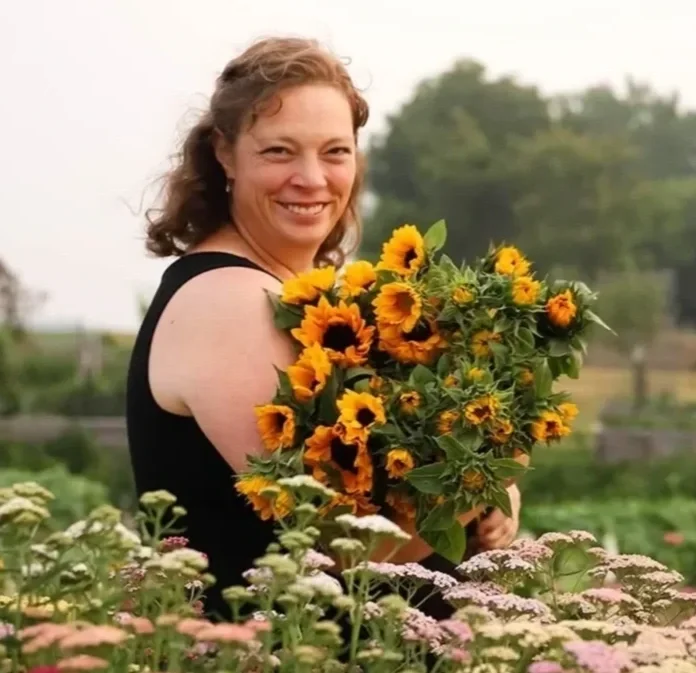 Flower farmer Ruth Ann stands in the field of flowers holding a bunch of sunflowers