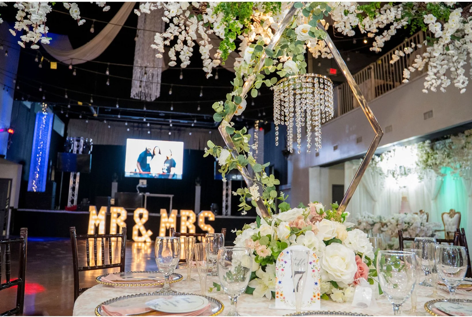 Elegant wedding reception with floral centerpiece, lighting, and 'Mr & Mrs' marquee lights in the background.
