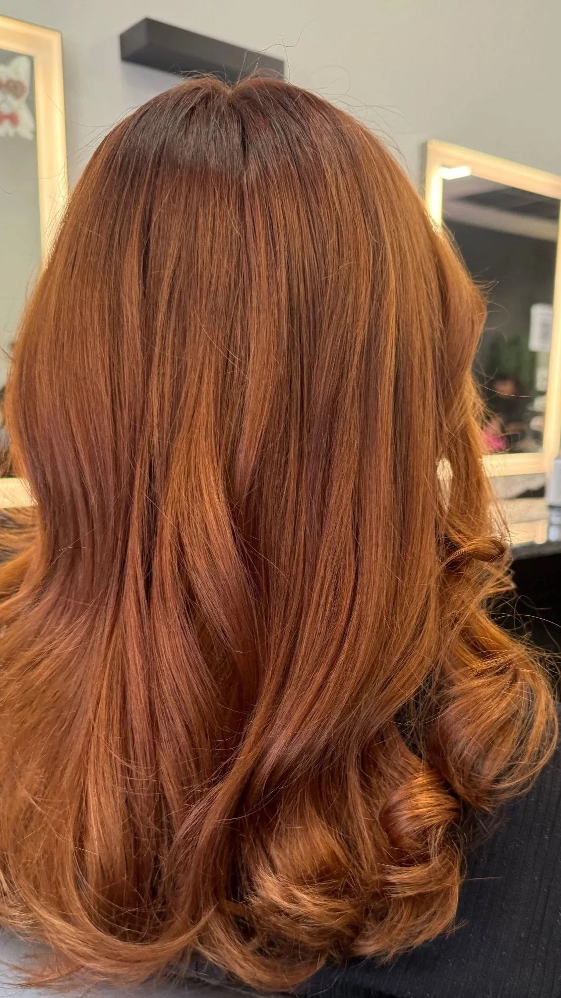 A young woman with long red wavy hair posing in front of a green leafy wall with a neon sign that says 'Pink Crush' in pink and purple letters.