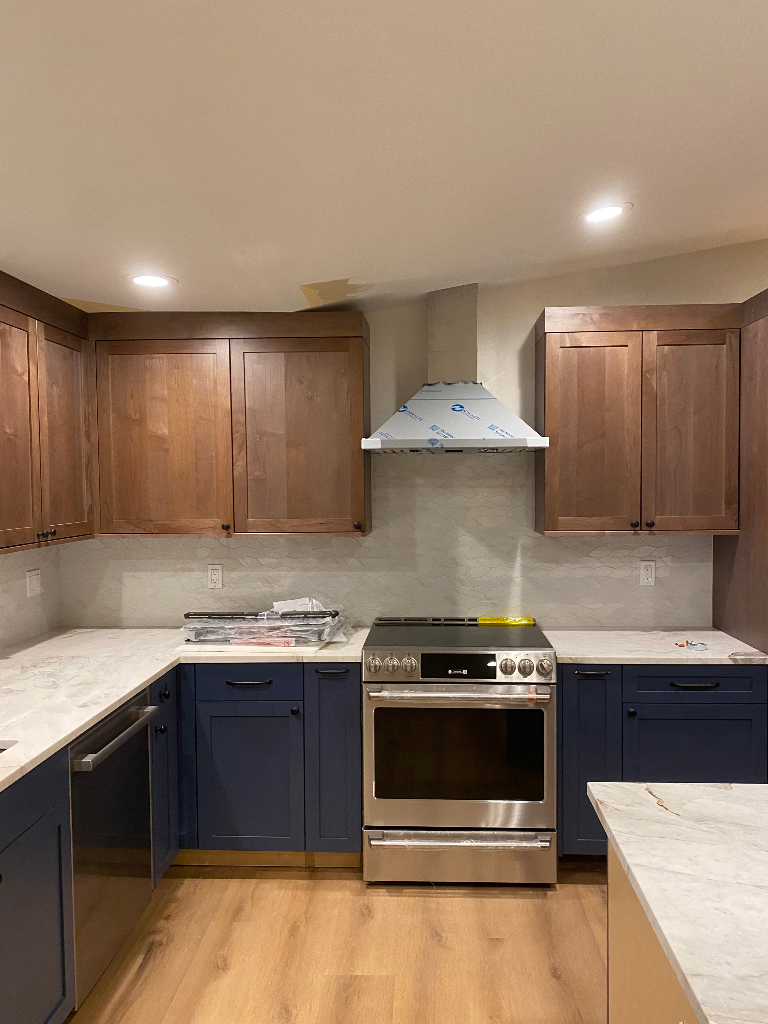 Kitchen with wooden cabinets, stainless steel oven, blue lower cabinets, and light-colored countertops, in progress of renovation.