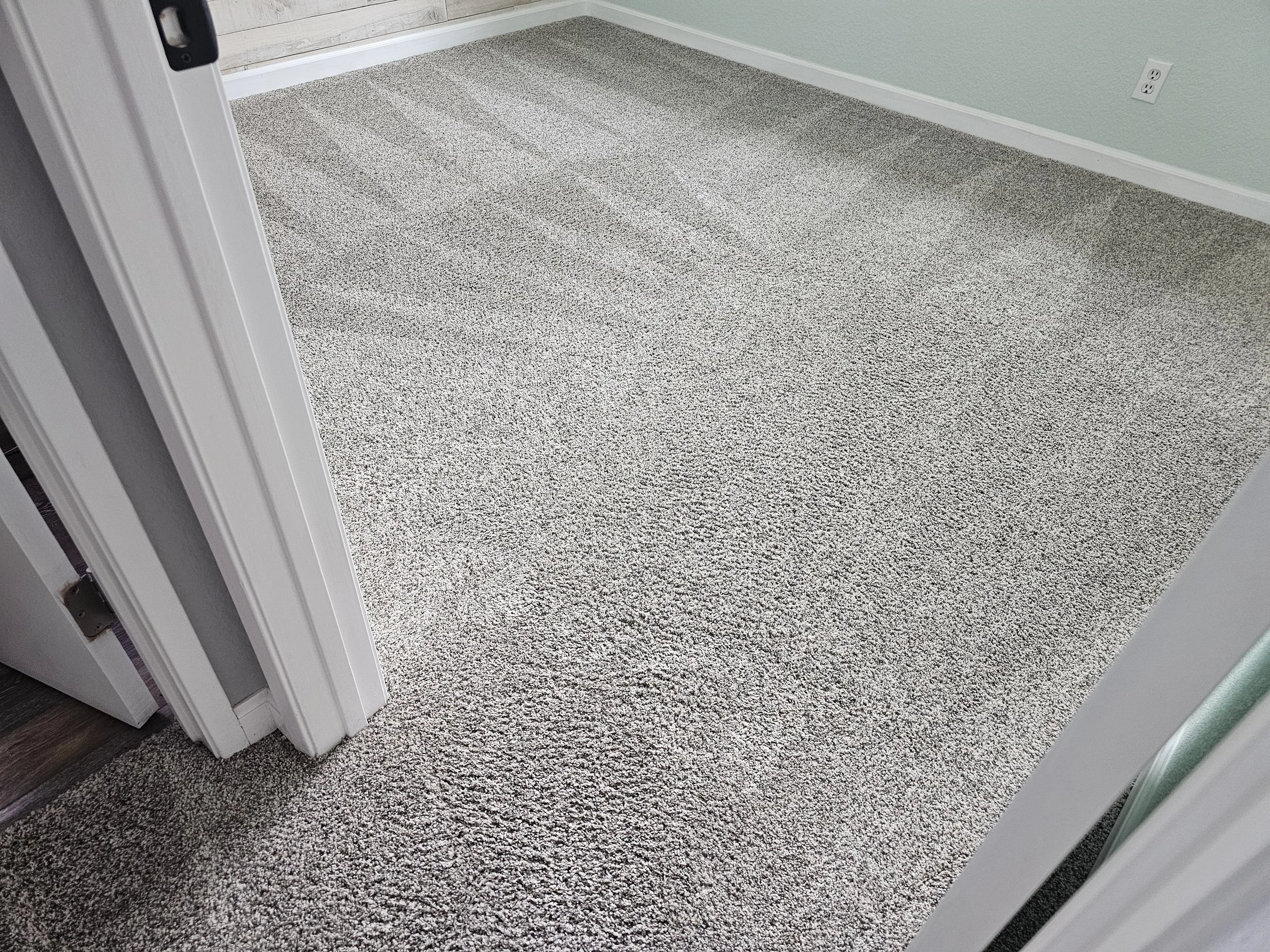 A room with a beige patterned carpet, a green wall, a white doorframe, and a visible white electrical outlet on the wall.