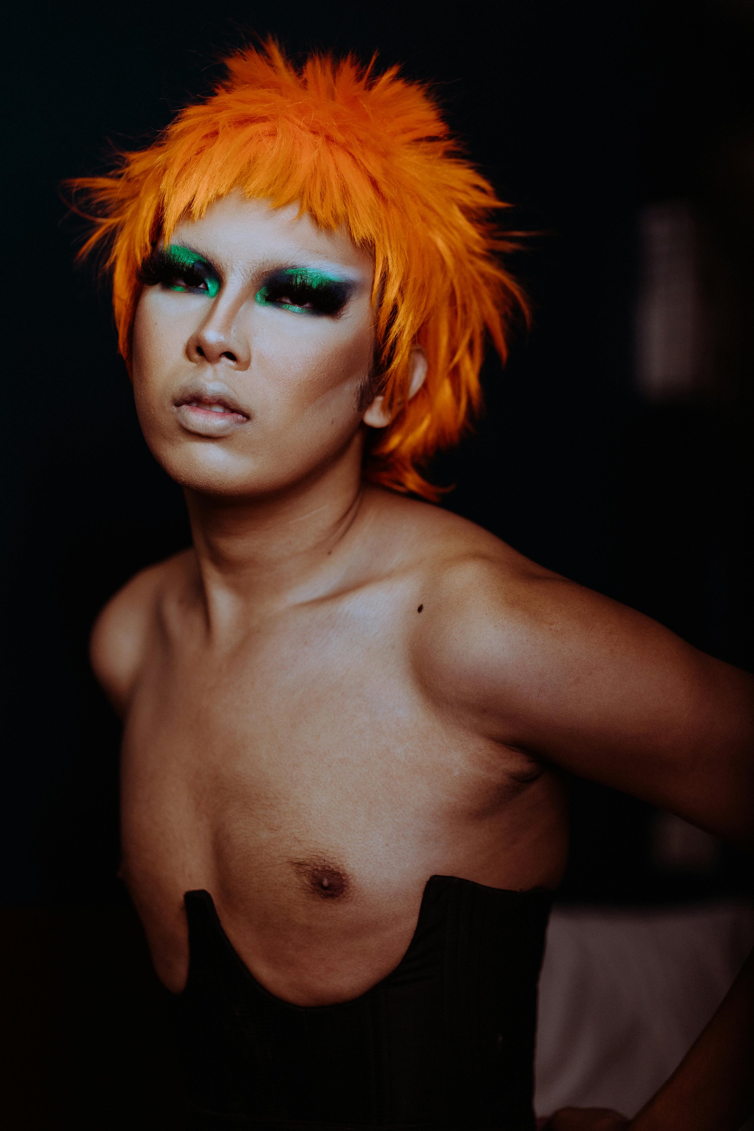 A Queer individual with colorful makeup posing for the camera.