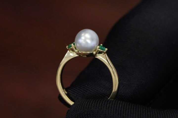 Handmade from Raw Kalgoorlie and Leonora Gold Nuggets from Western Australia, this sentimental ring features a lustrous South Sea Pearl embraced by two Natural Green Emeralds. The cup of the pearl bears symbols of unity, with women and man engravings