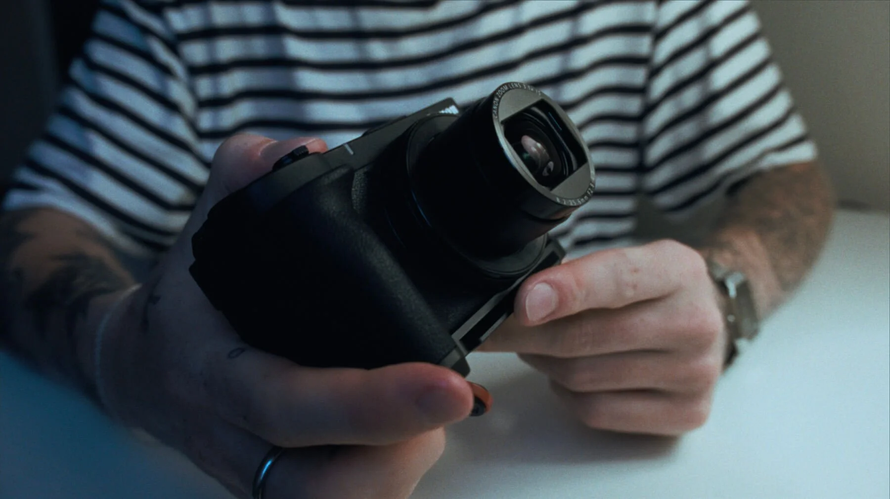 canon powershot v1 in a tattooed person hands wearing a striped shirt