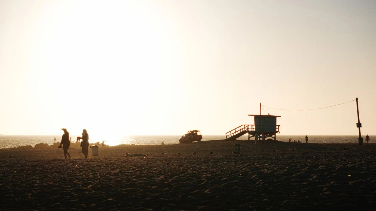 two silhouetted people walk away from sunset and lifeguard tower on beach