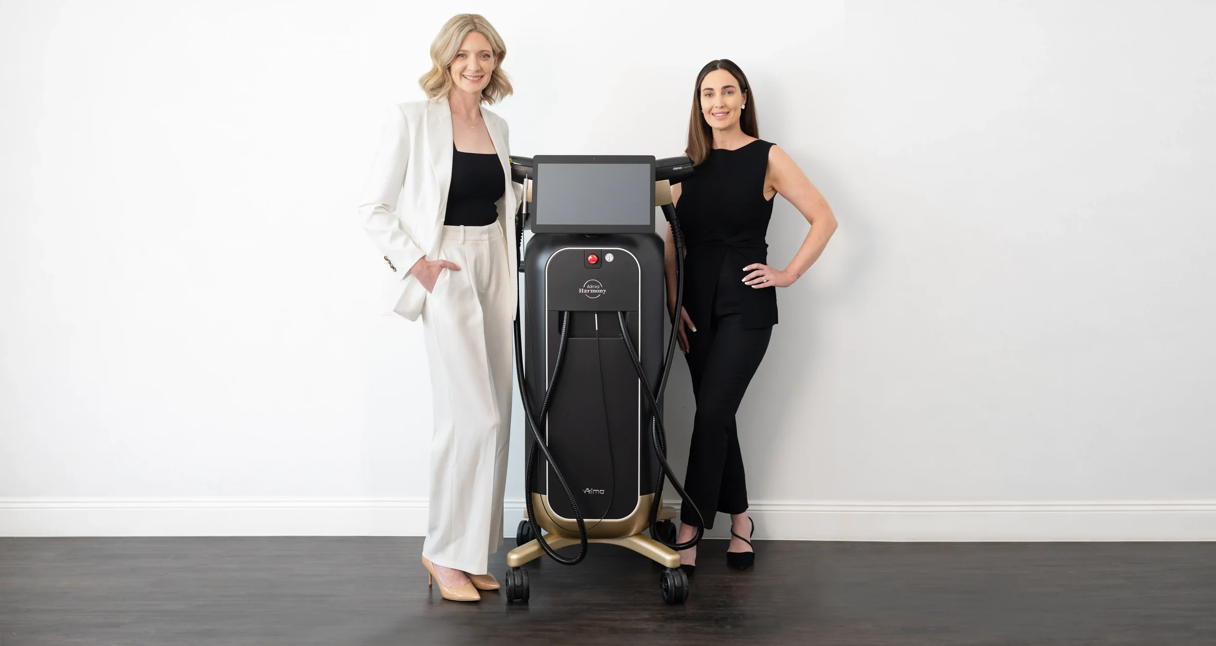 Dr Samantha Davidson and dermal clinician Tahlia standing with the ALMA Harmony machine in clinic at the Gold Coast Dermatology Clinic.