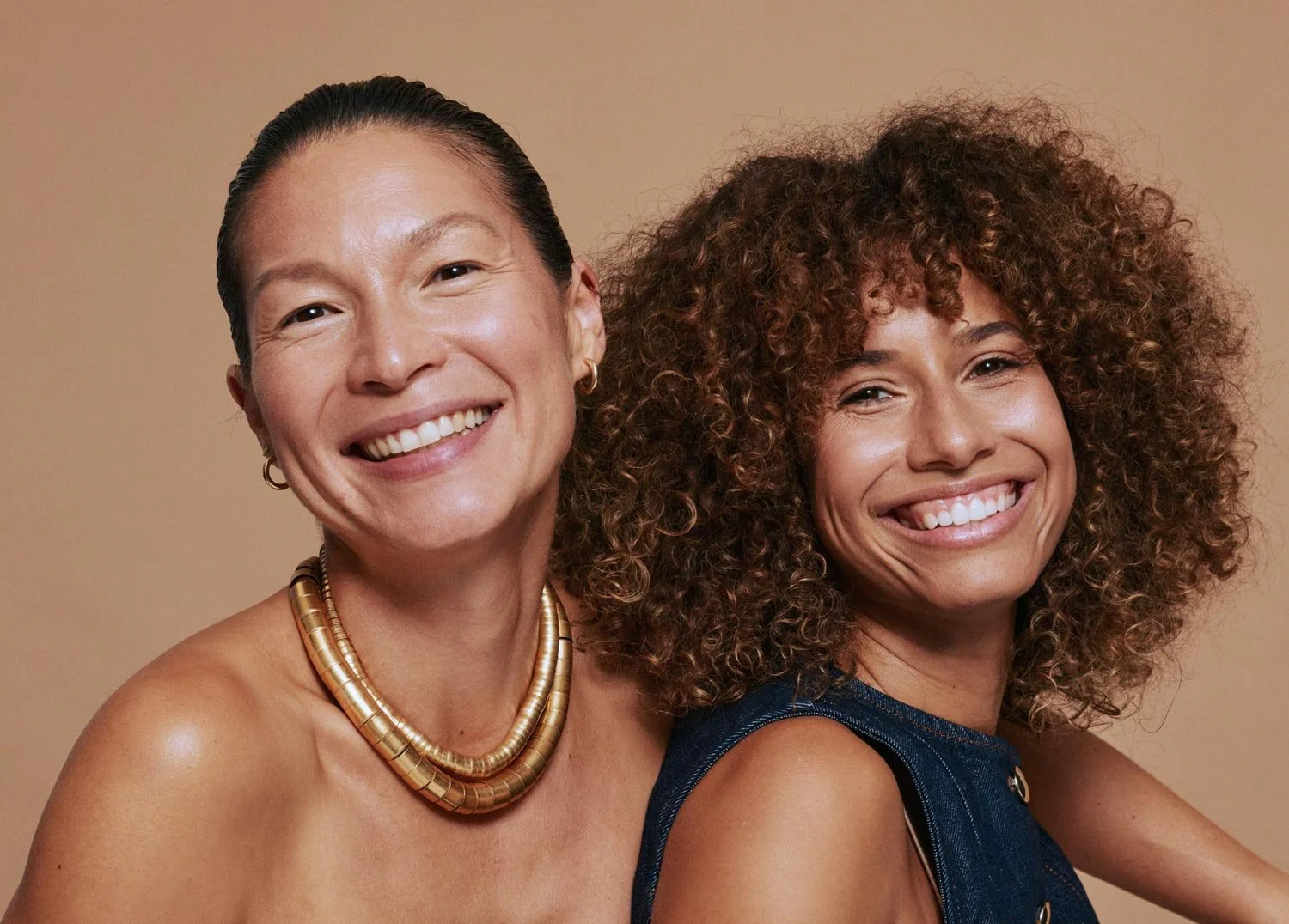 Two middle-aged women smiling with glowing, healthy skin.