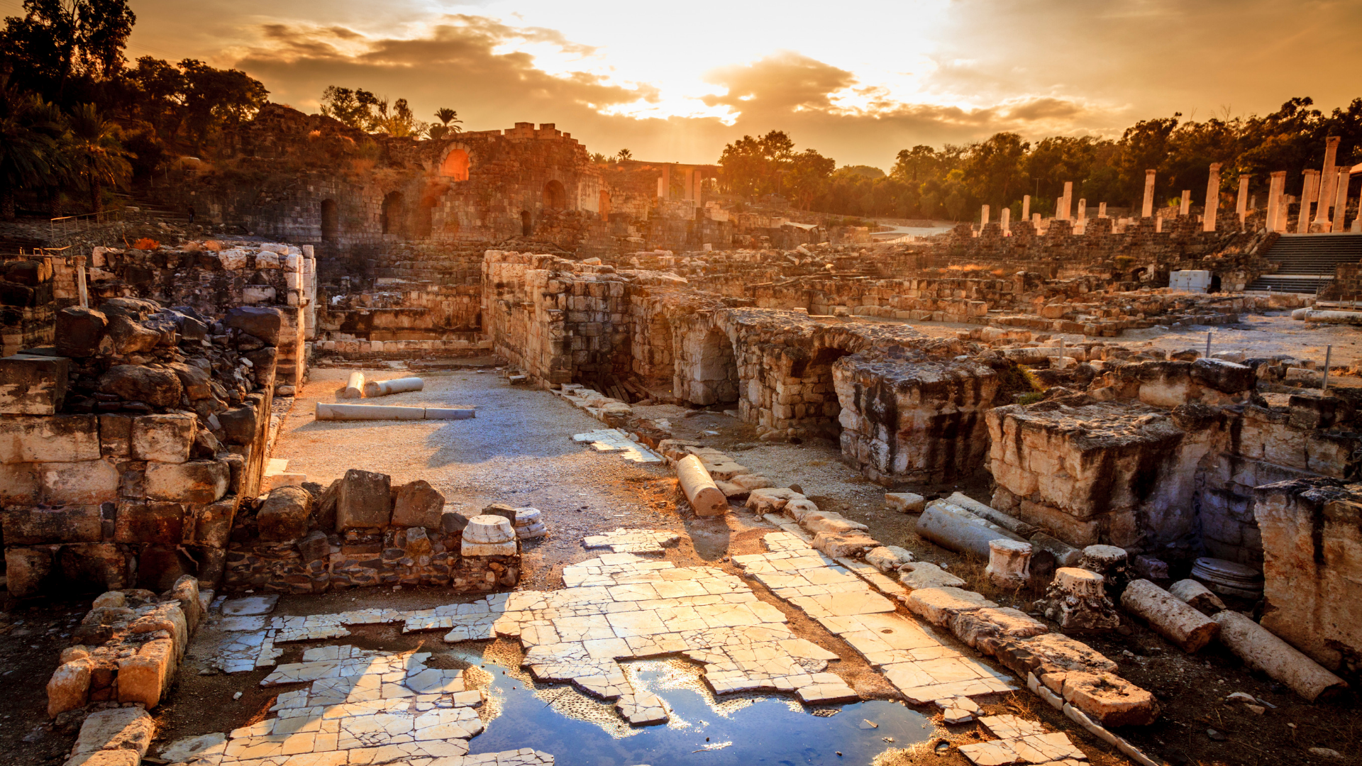 Ancient ruins at sunset with stone arches, columns, and scattered fallen stones.