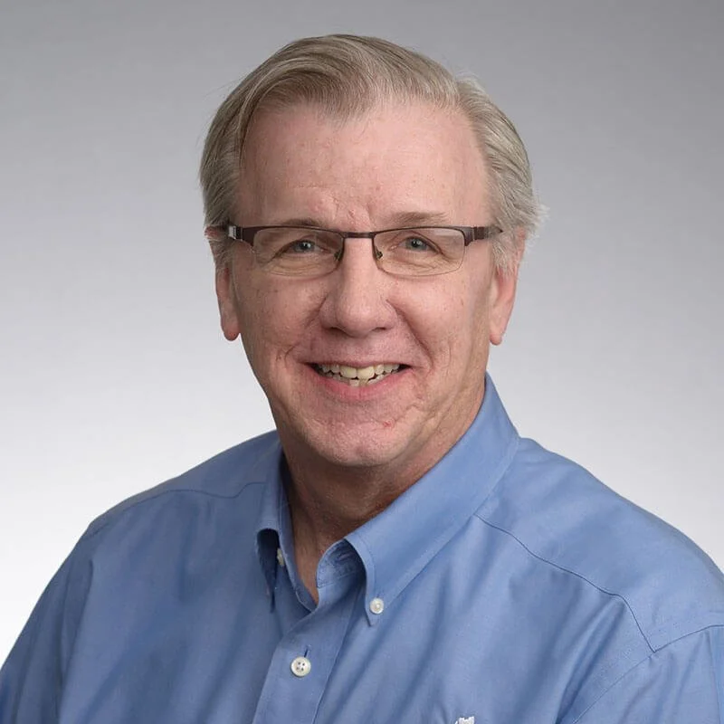 Black and white photo of a smiling middle-aged man with glasses, wearing a button-up shirt.