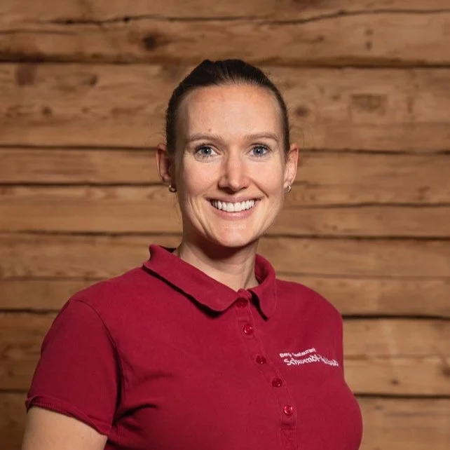 Person in rotem Polo-Shirt vor Holzwand, lächelnd.