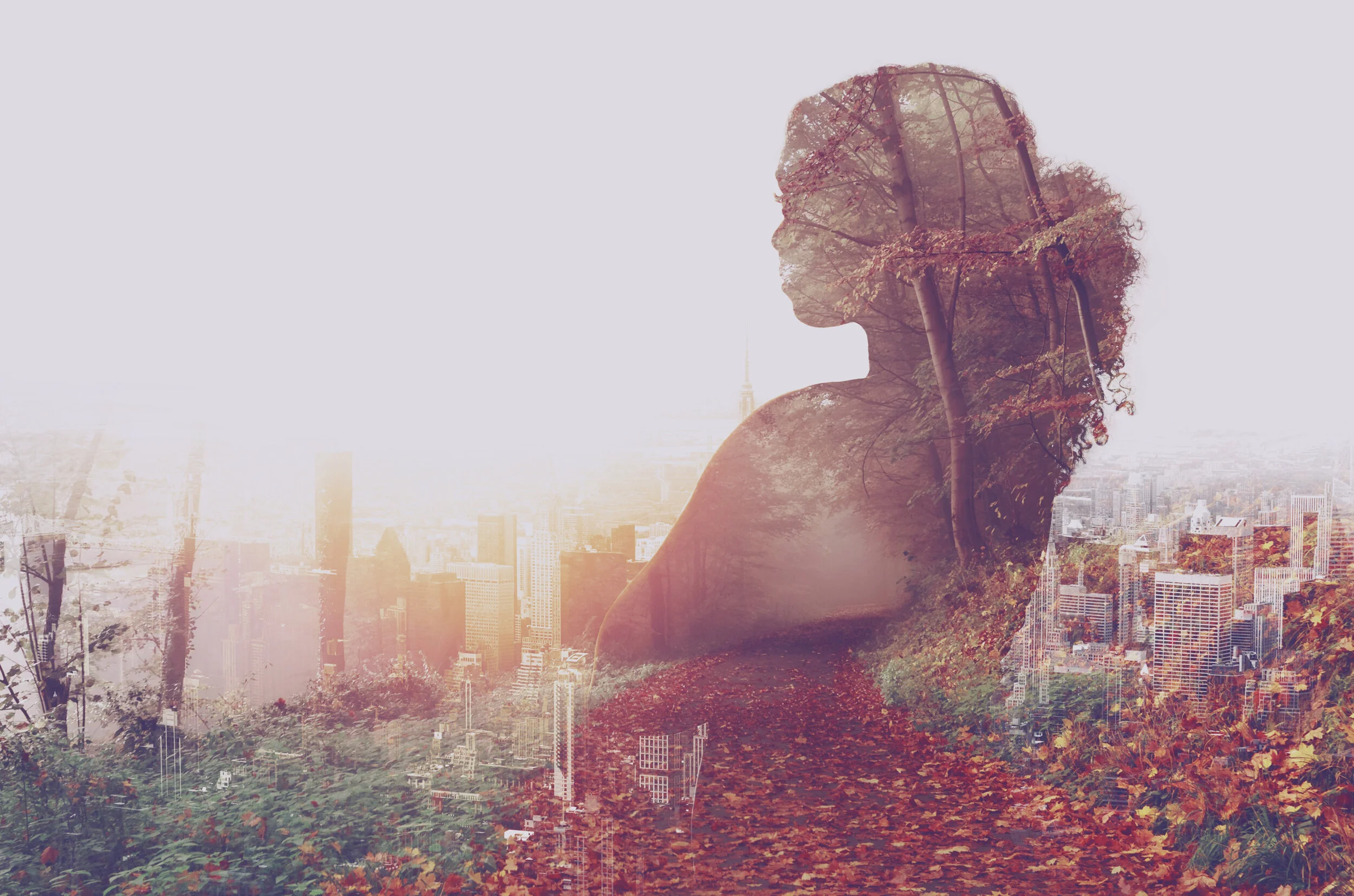 Double exposure of a young woman with autumn foliage and a city skyline.