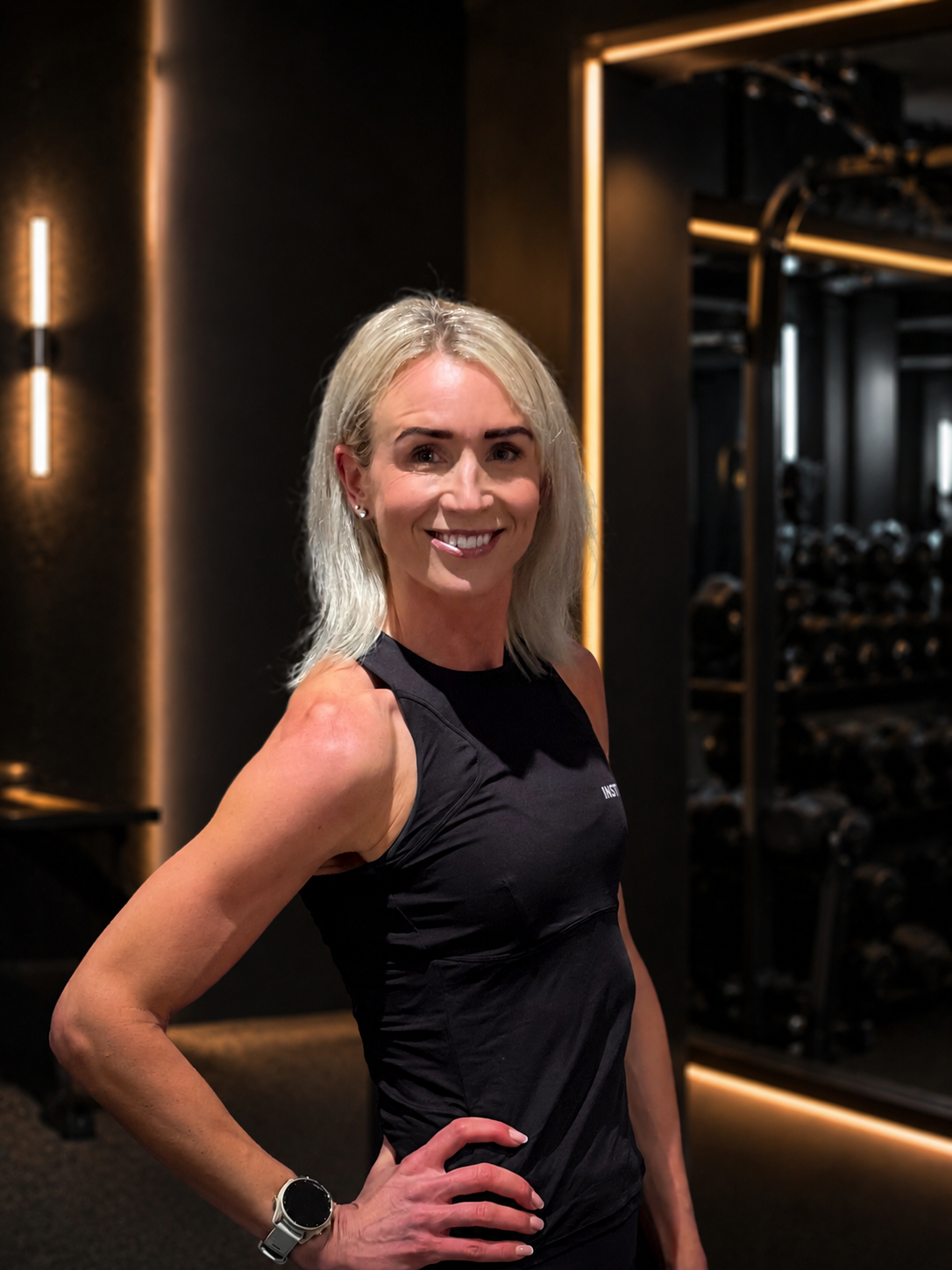 Kvinna på gymmet i lila linne håller en skivstång och ler.