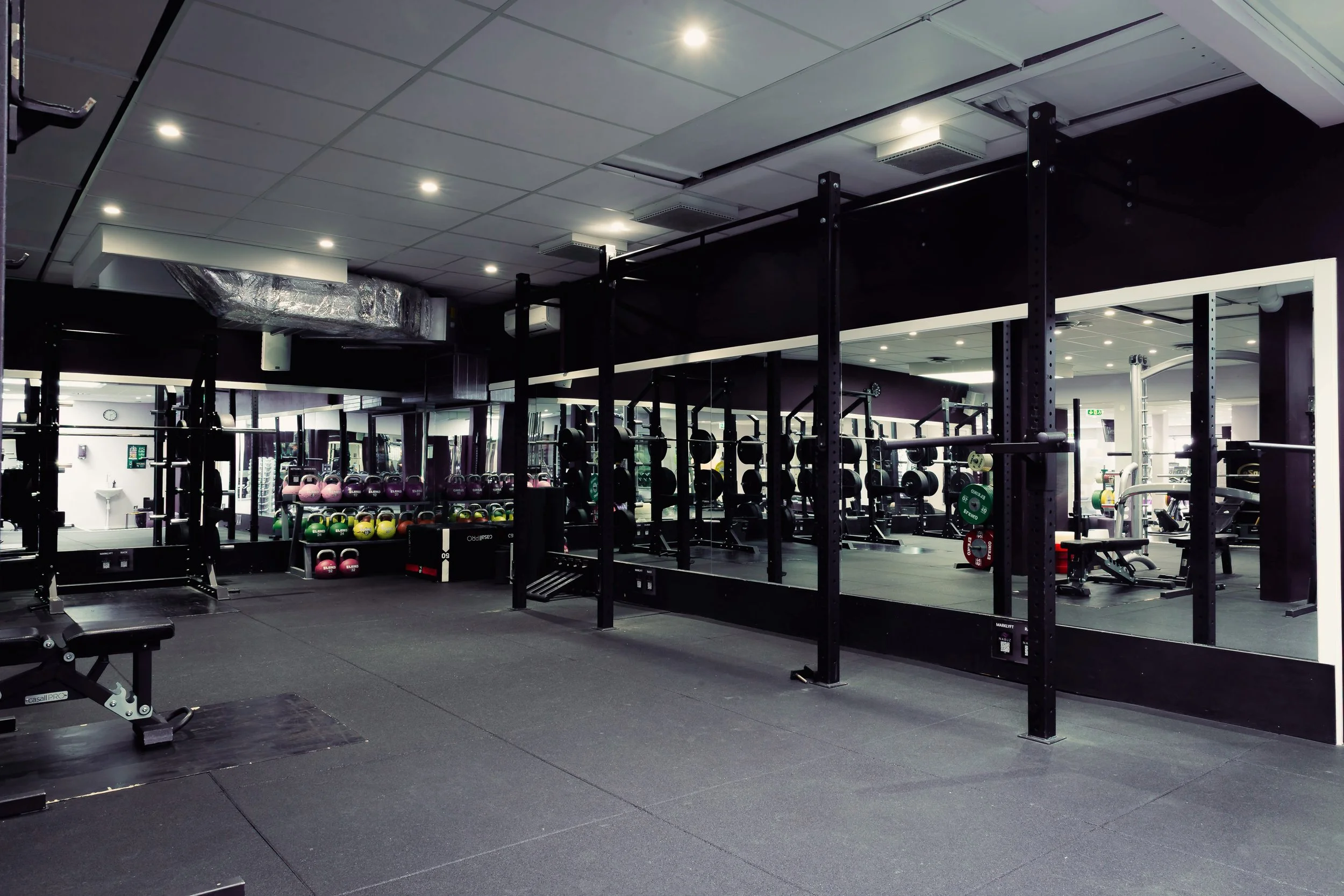 Gym med vikter och squatställ, spegel i bakgrunden.